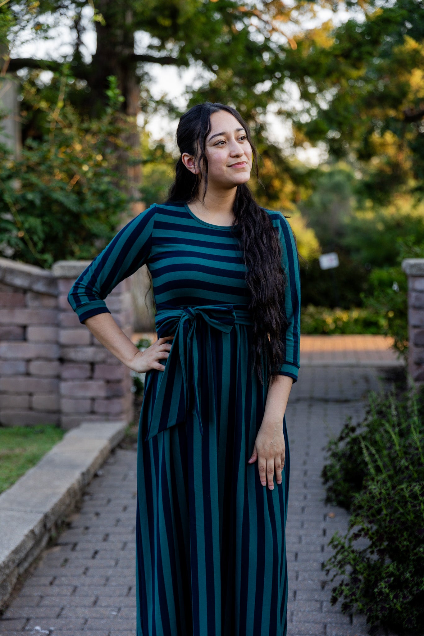 Model wearing the Nuggles® Adelia Dress, a modest striped maxi dress with waist tie and ¾ sleeves.