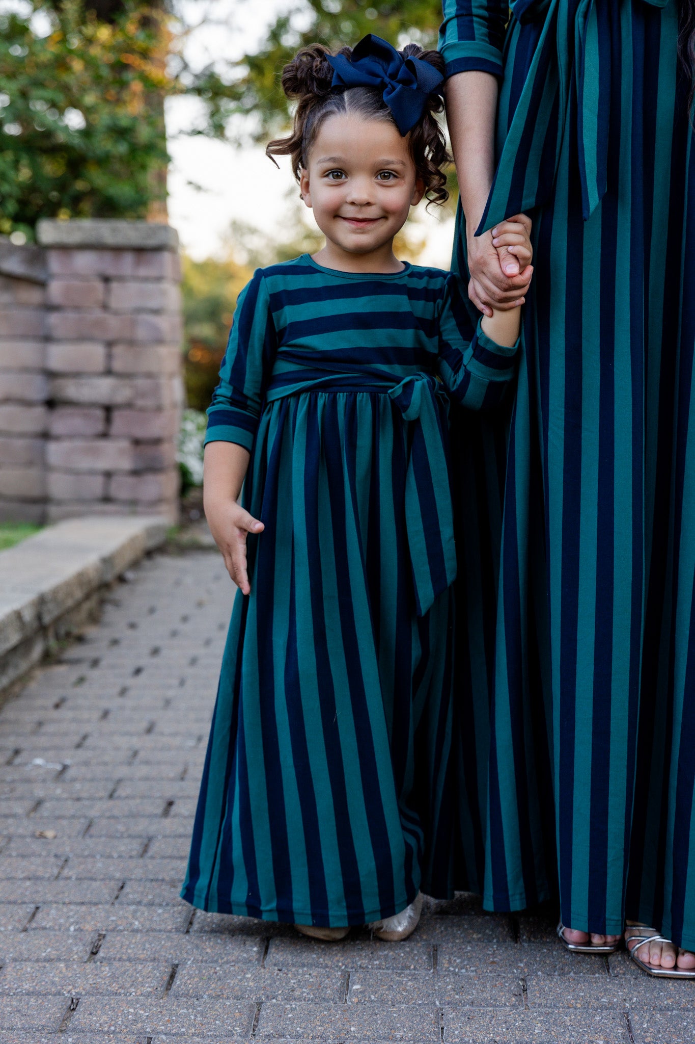 Young girl wearing the Nuggles® Girls Adelia Dress — a modest striped maxi dress with bow tie waist.