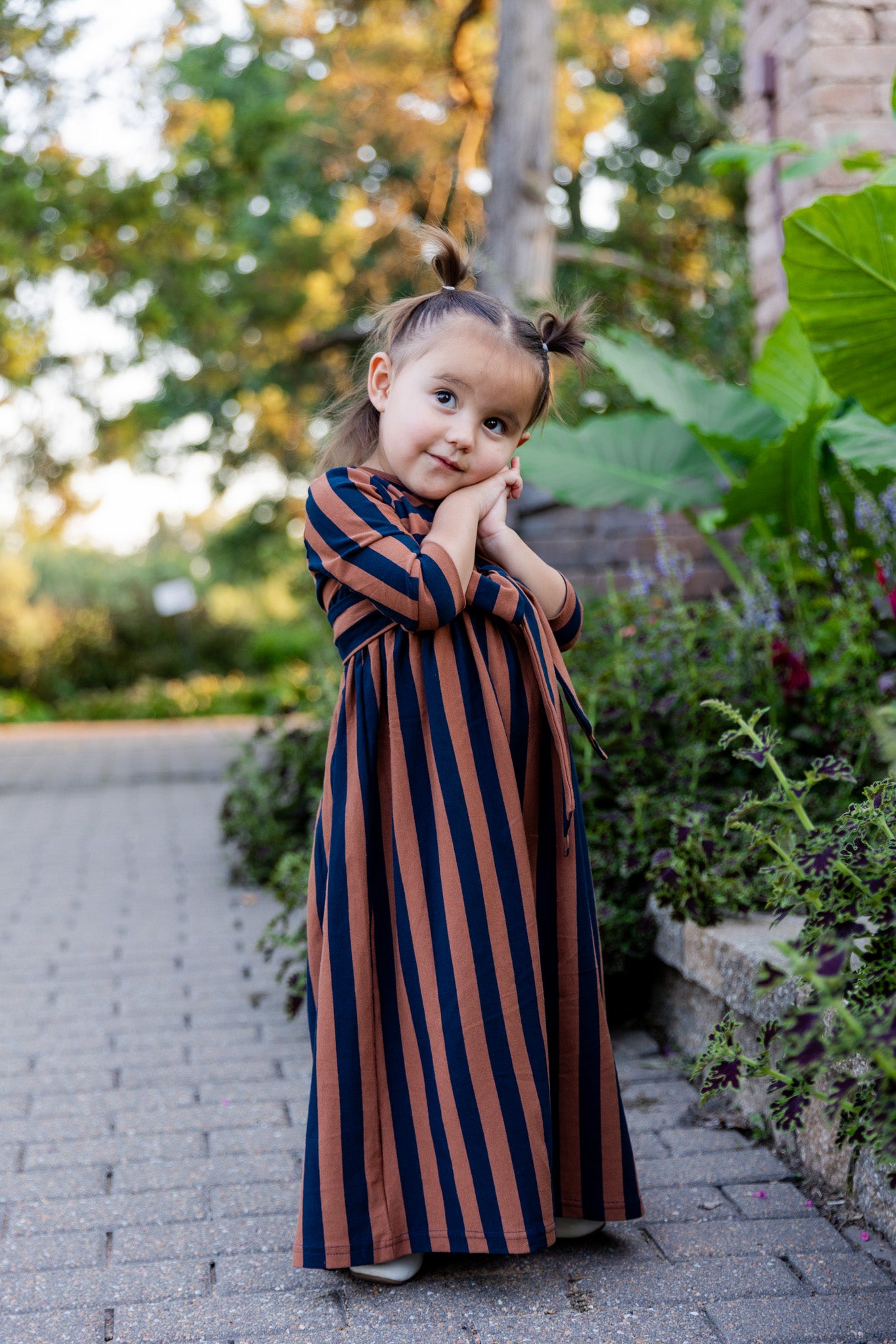 Young girl wearing the Nuggles® Girls Adelia Dress — a modest striped maxi dress with bow tie waist.