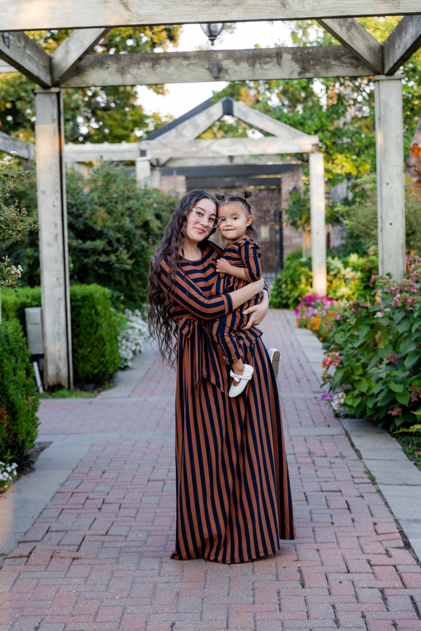Young girl wearing the Nuggles® Girls Adelia Dress — a modest striped maxi dress with bow tie waist.