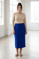 Woman wearing a beige top and blue skirt in a bright room