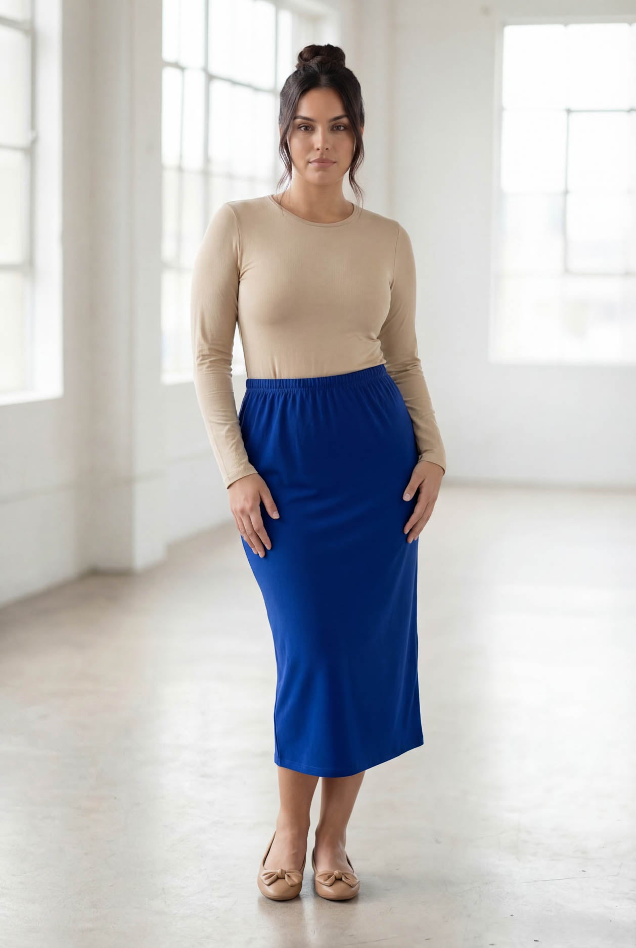 Woman wearing a beige top and blue skirt in a bright room