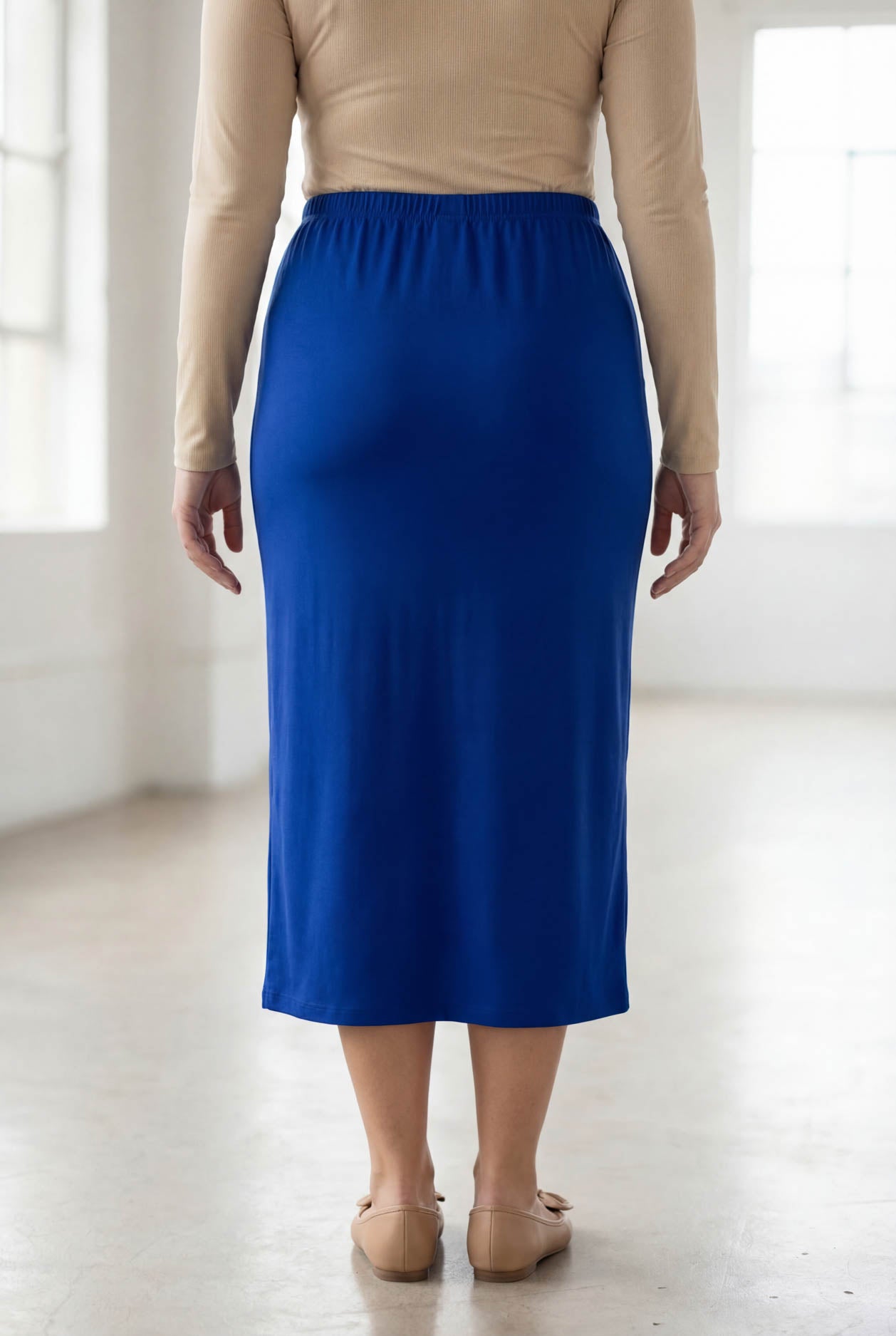 Person wearing a blue skirt and beige top in a bright room
