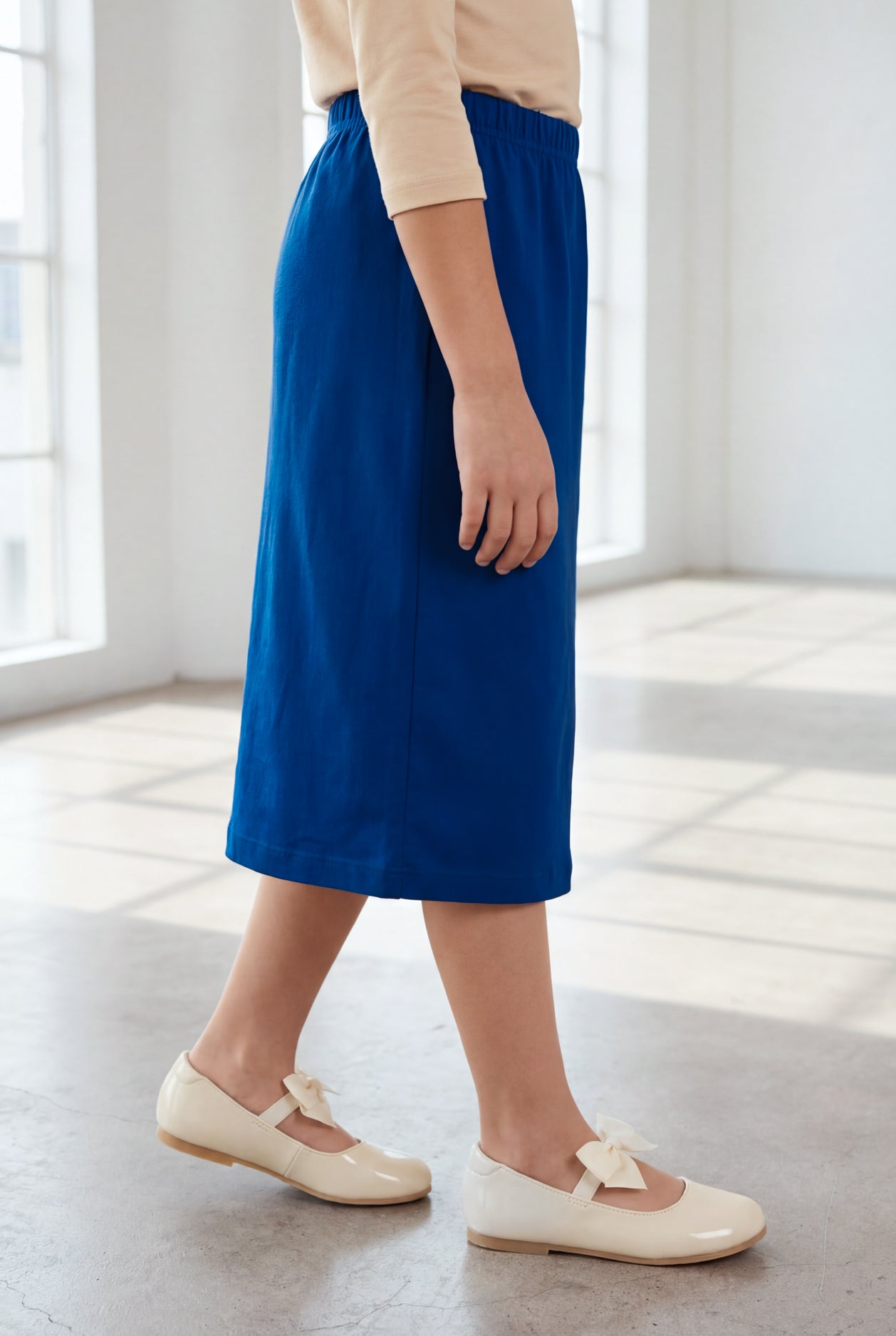 Young girl wearing a modest midi length skirt in dark royal with a beige colored 3/4 length sleeve shirt. 
