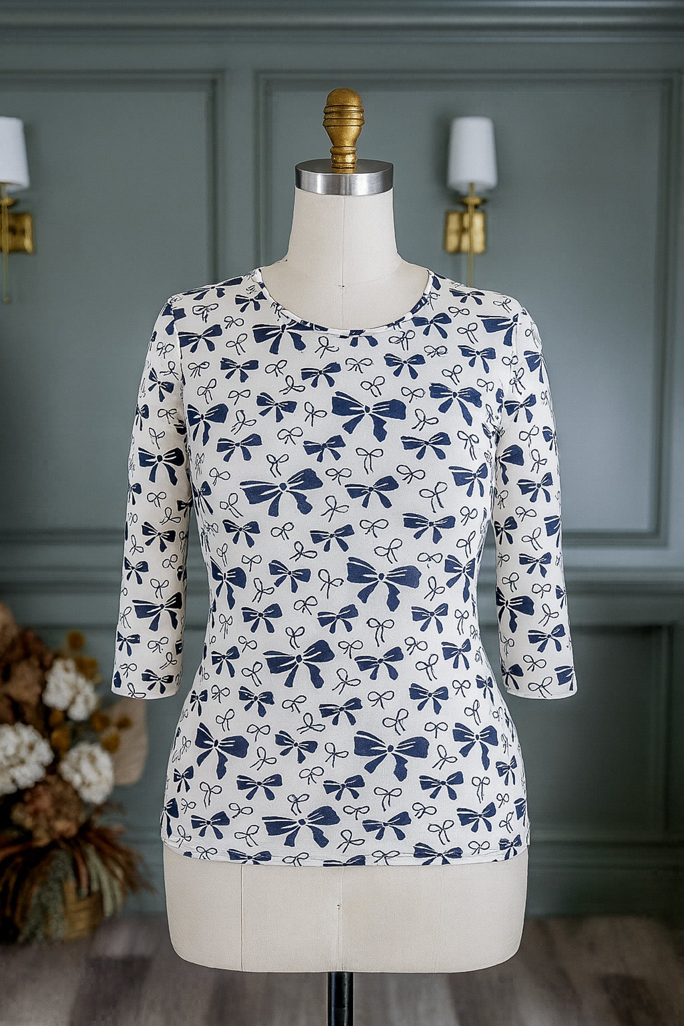 White blouse with blue bow pattern on a mannequin against a gray wall.