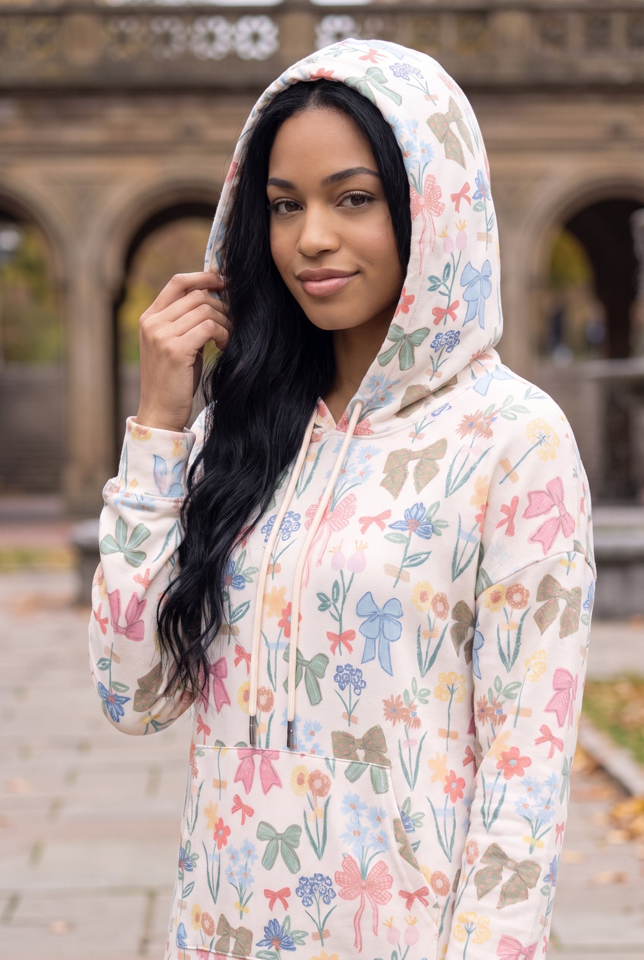 Nuggles® Hoodie Dress in Garden Party worn with the hood up, bow and floral print on cream