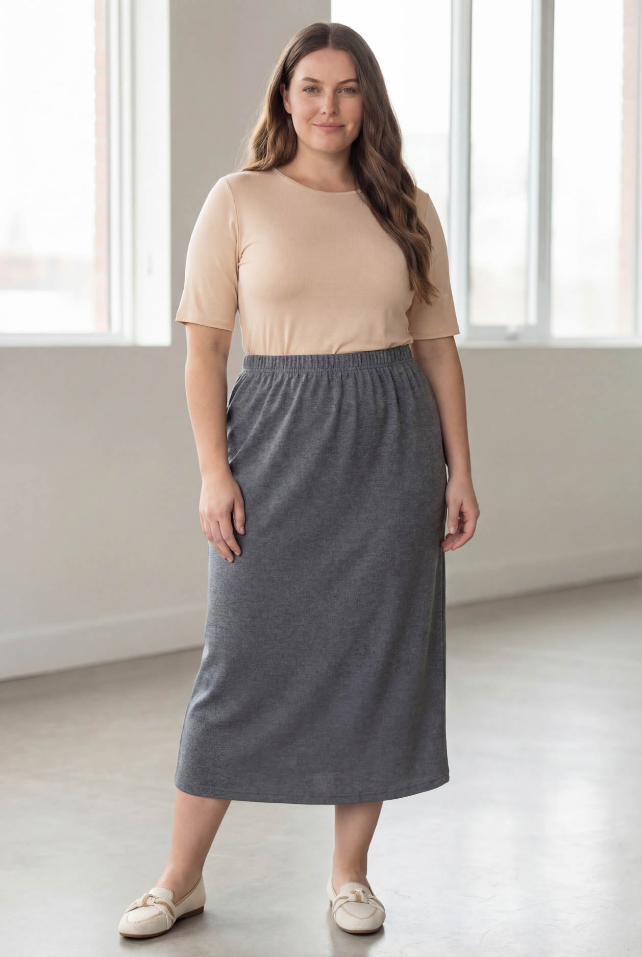 Woman wearing a beige top and gray skirt in a bright room.