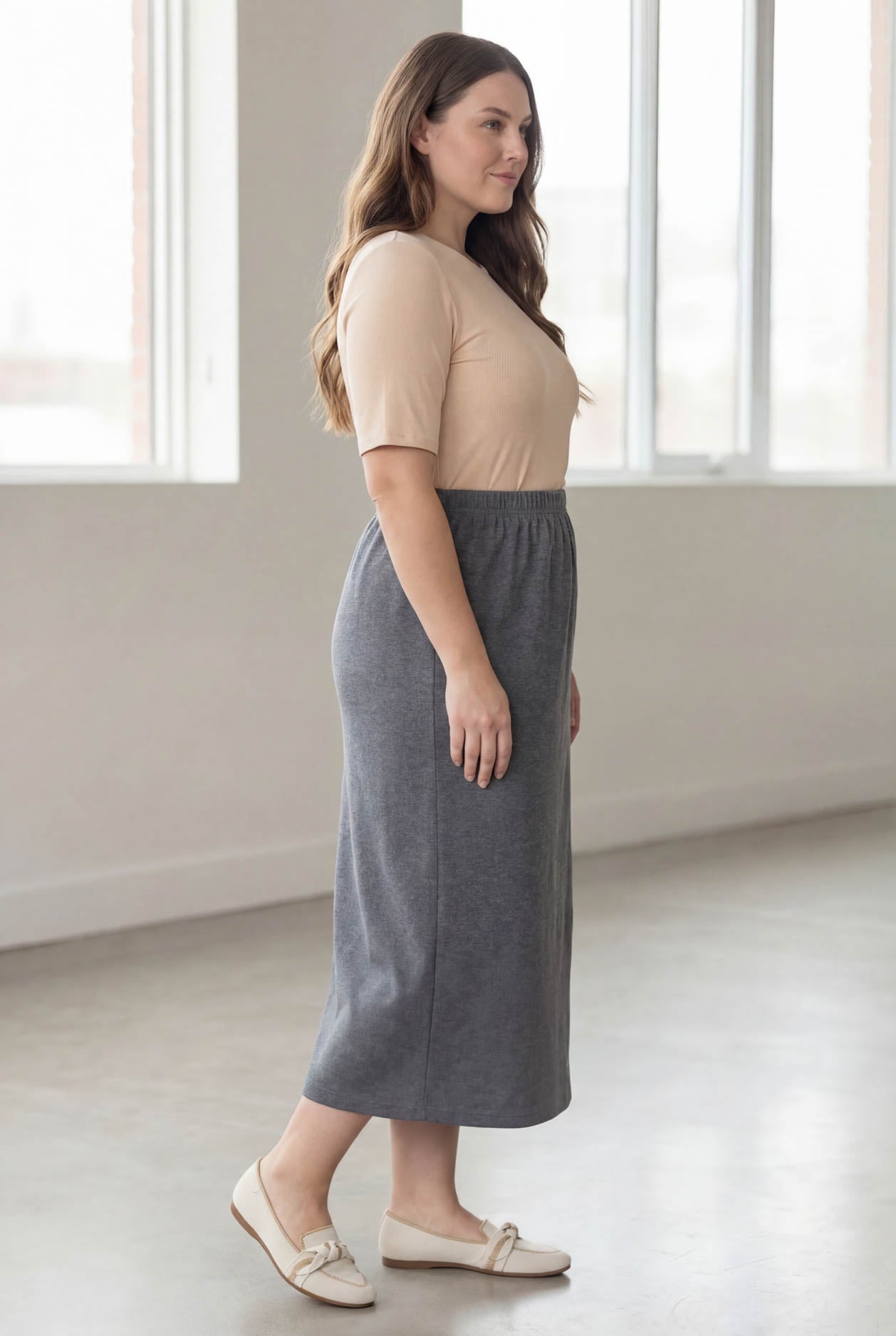 Woman wearing a beige top and gray skirt in a bright room.