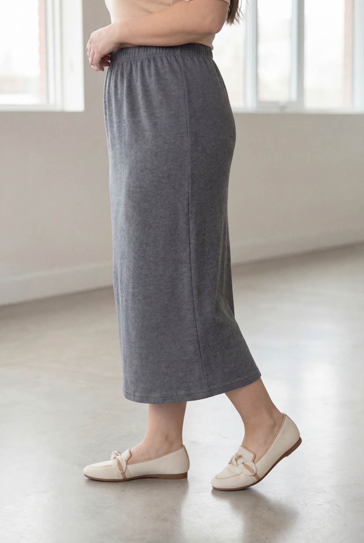 Woman wearing a beige top and gray skirt in a bright room.