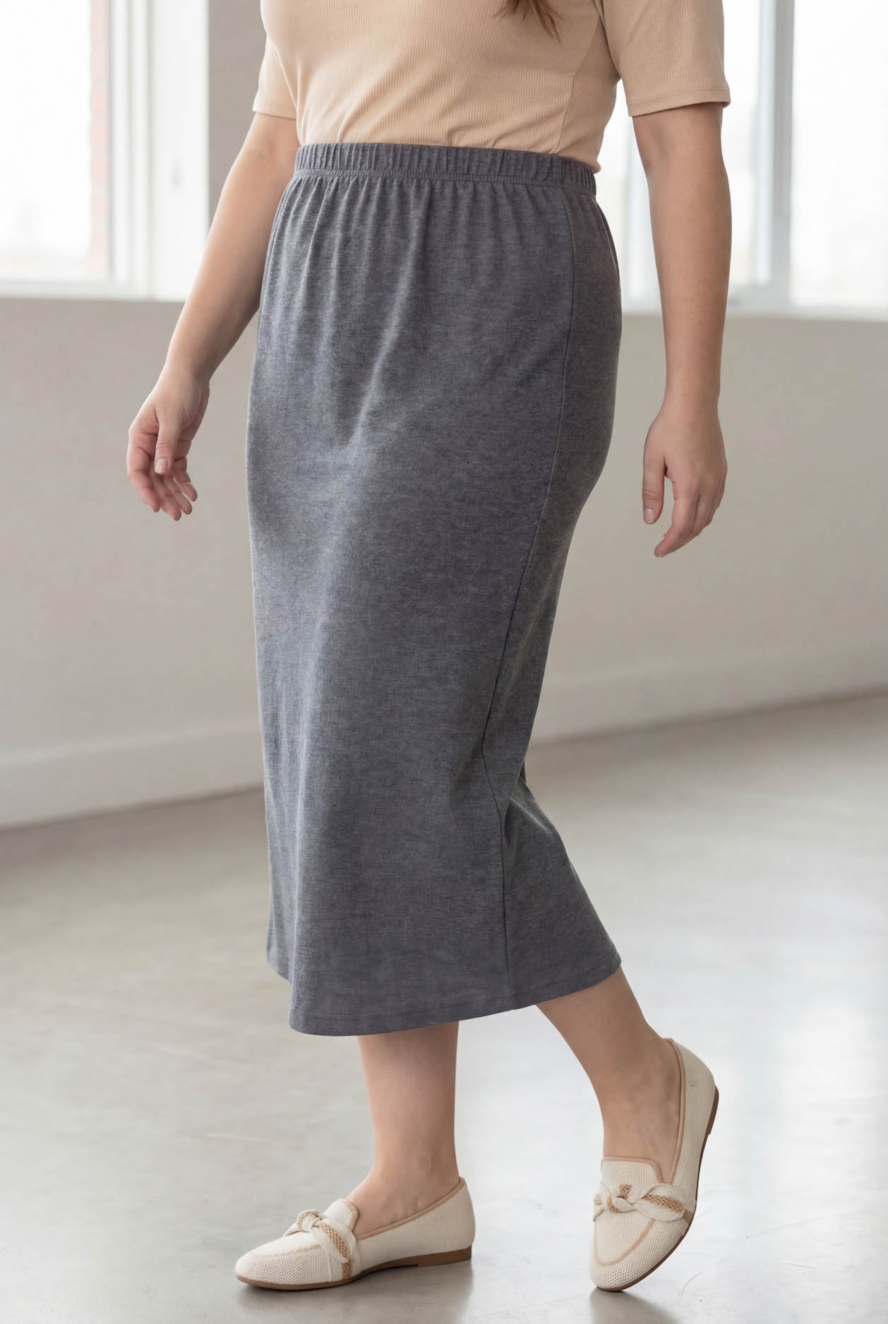 Woman wearing a beige top and gray skirt in a bright room.