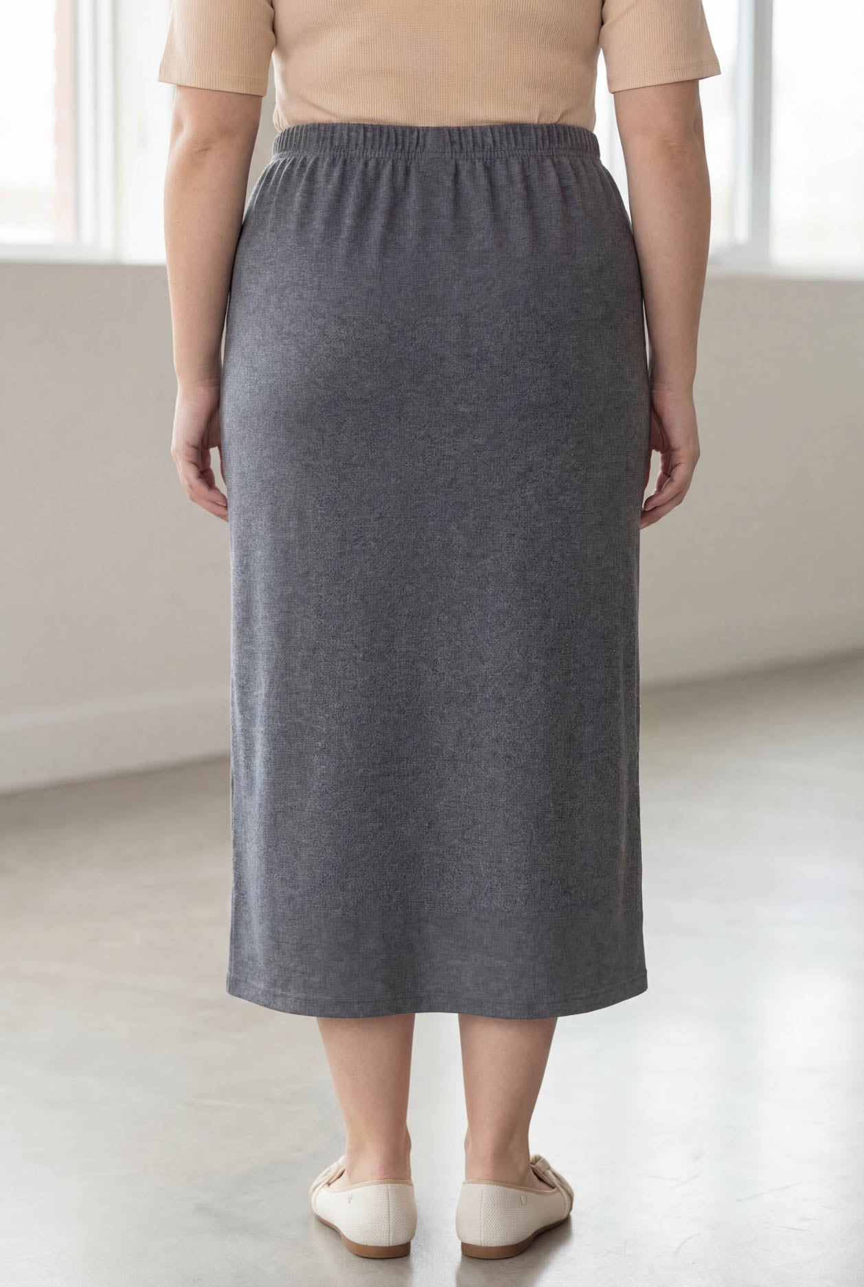 Woman wearing a beige top and gray skirt in a bright room.