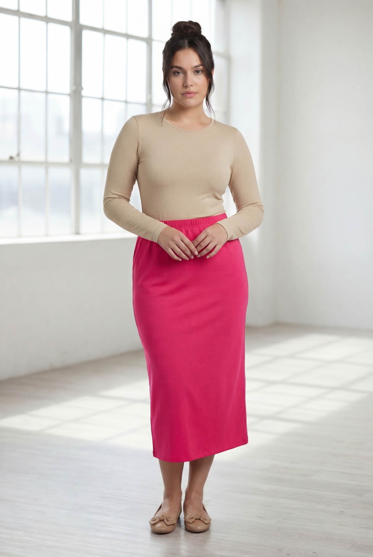 Woman wearing a beige top and pink skirt in a bright room.