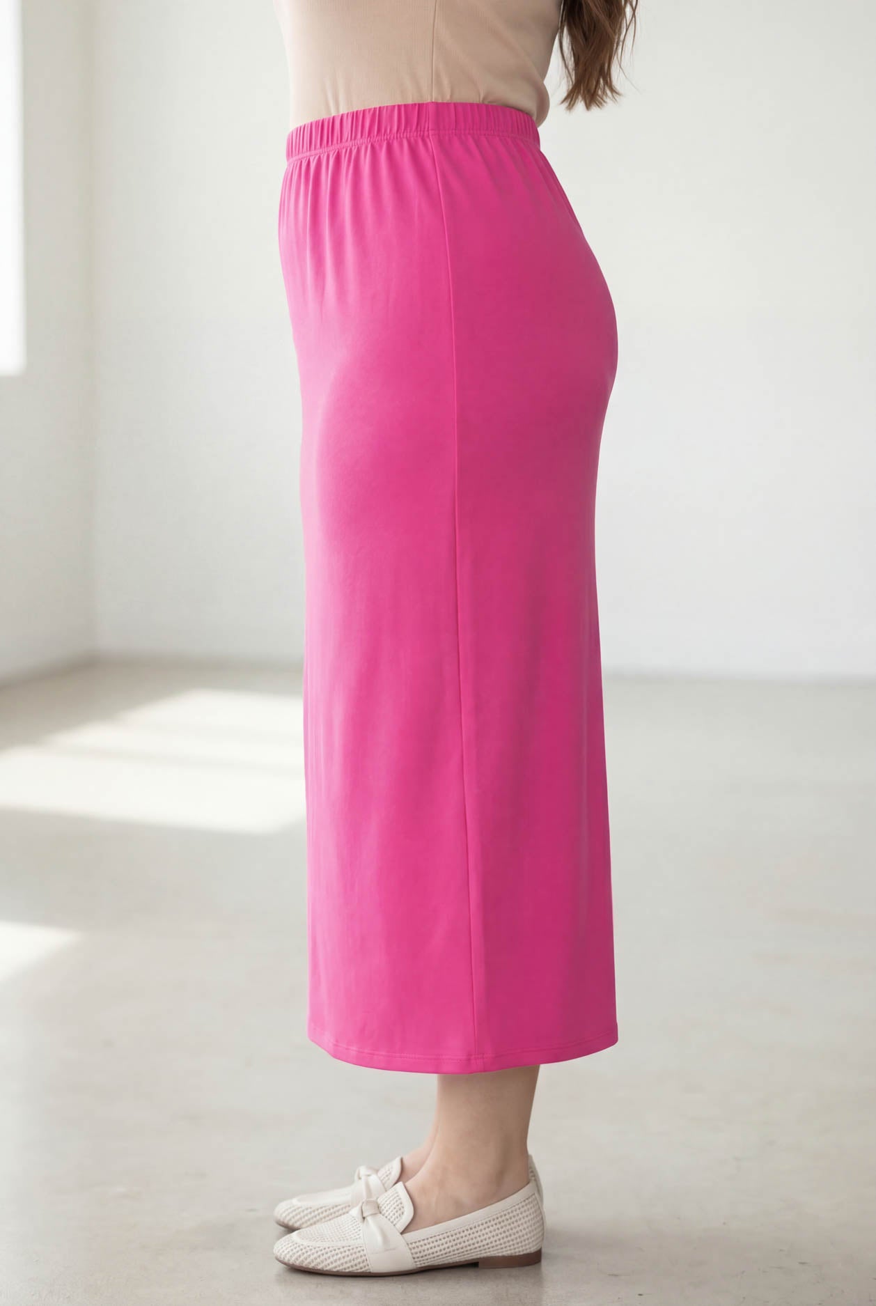 Woman wearing a beige top and pink skirt in a bright room.