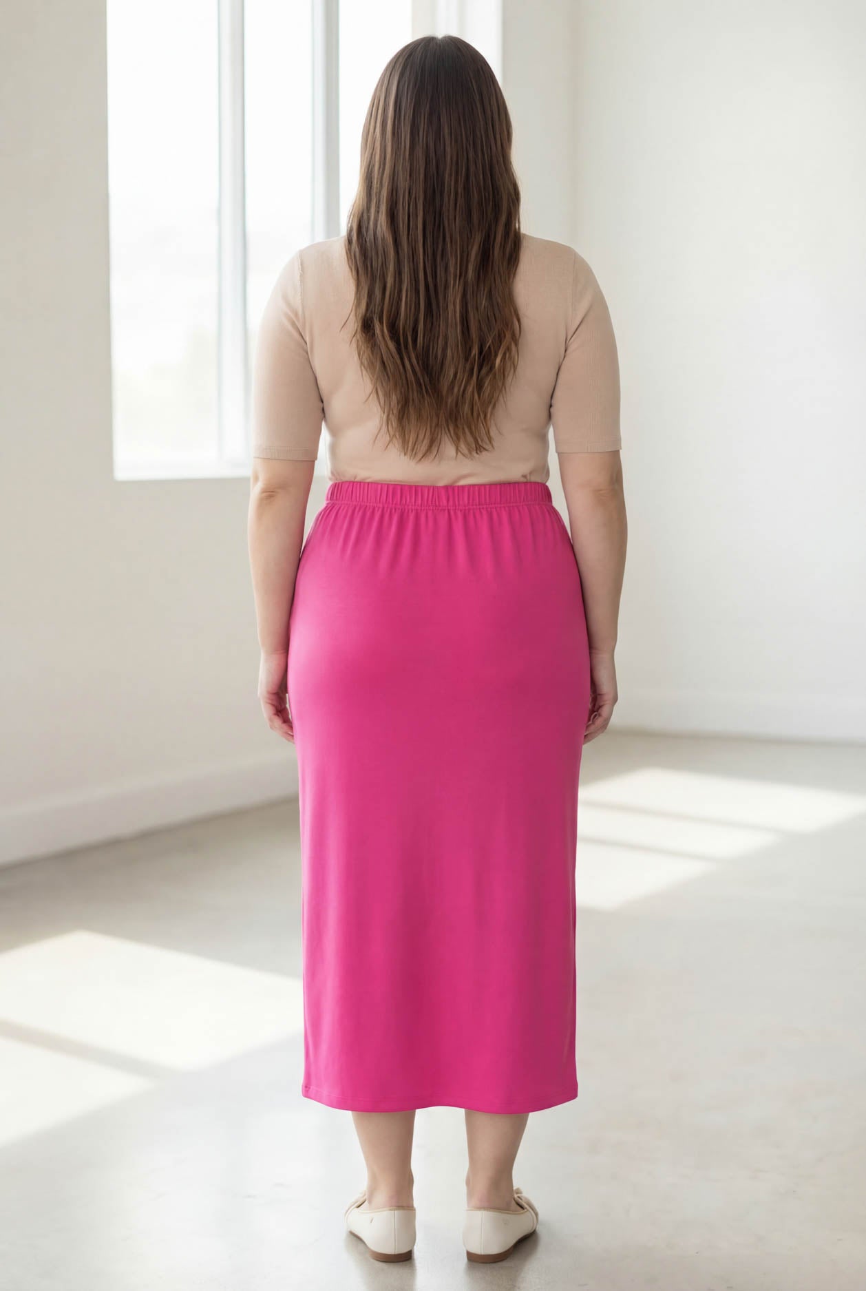 Woman wearing a beige top and pink skirt in a bright room.