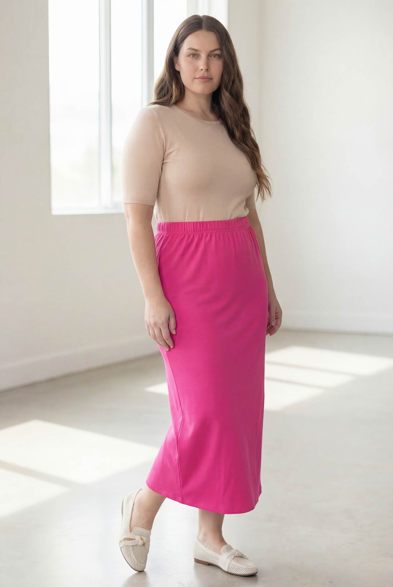 Woman wearing a beige top and pink skirt in a bright room.
