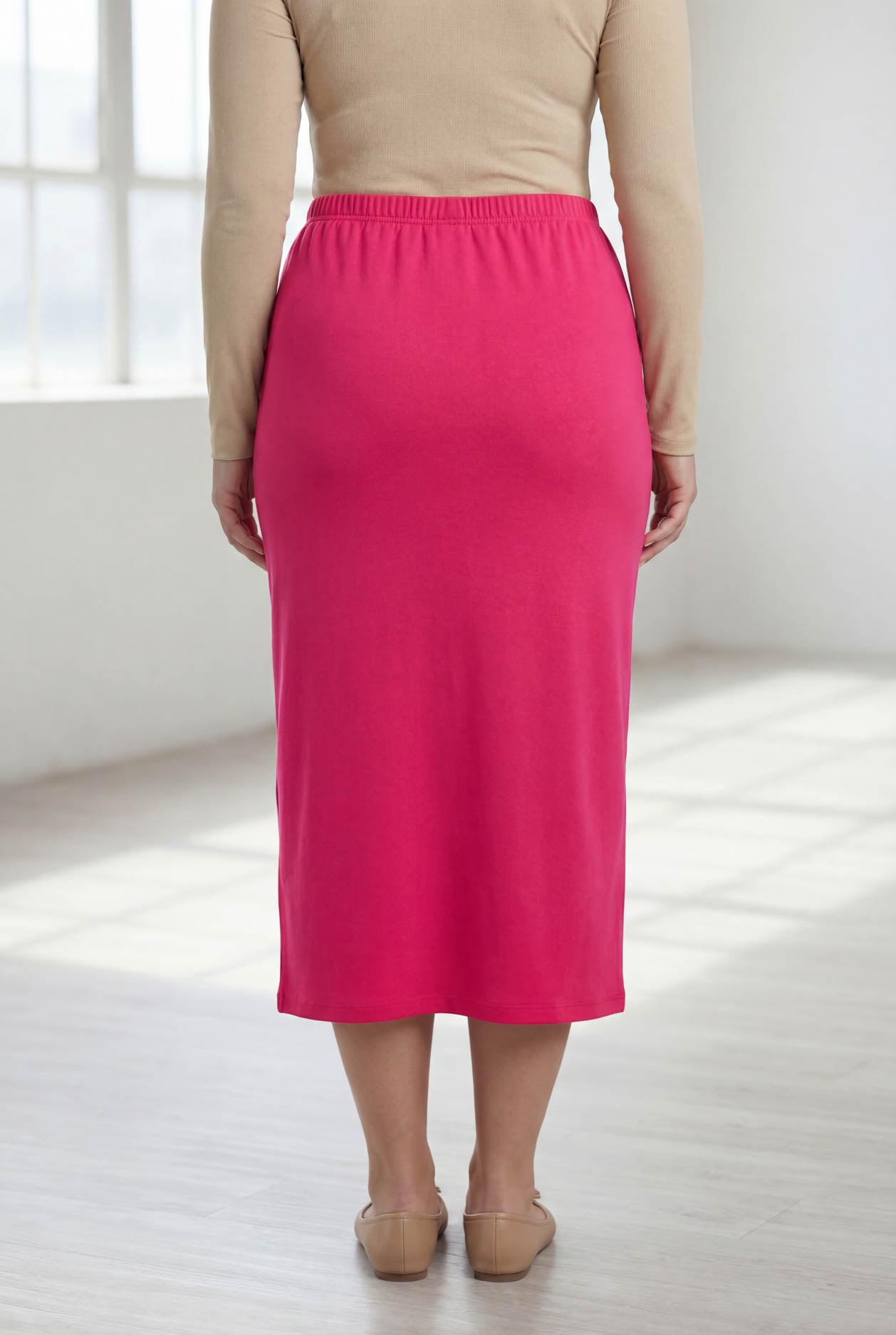 Person wearing a pink skirt and beige top in a bright room.