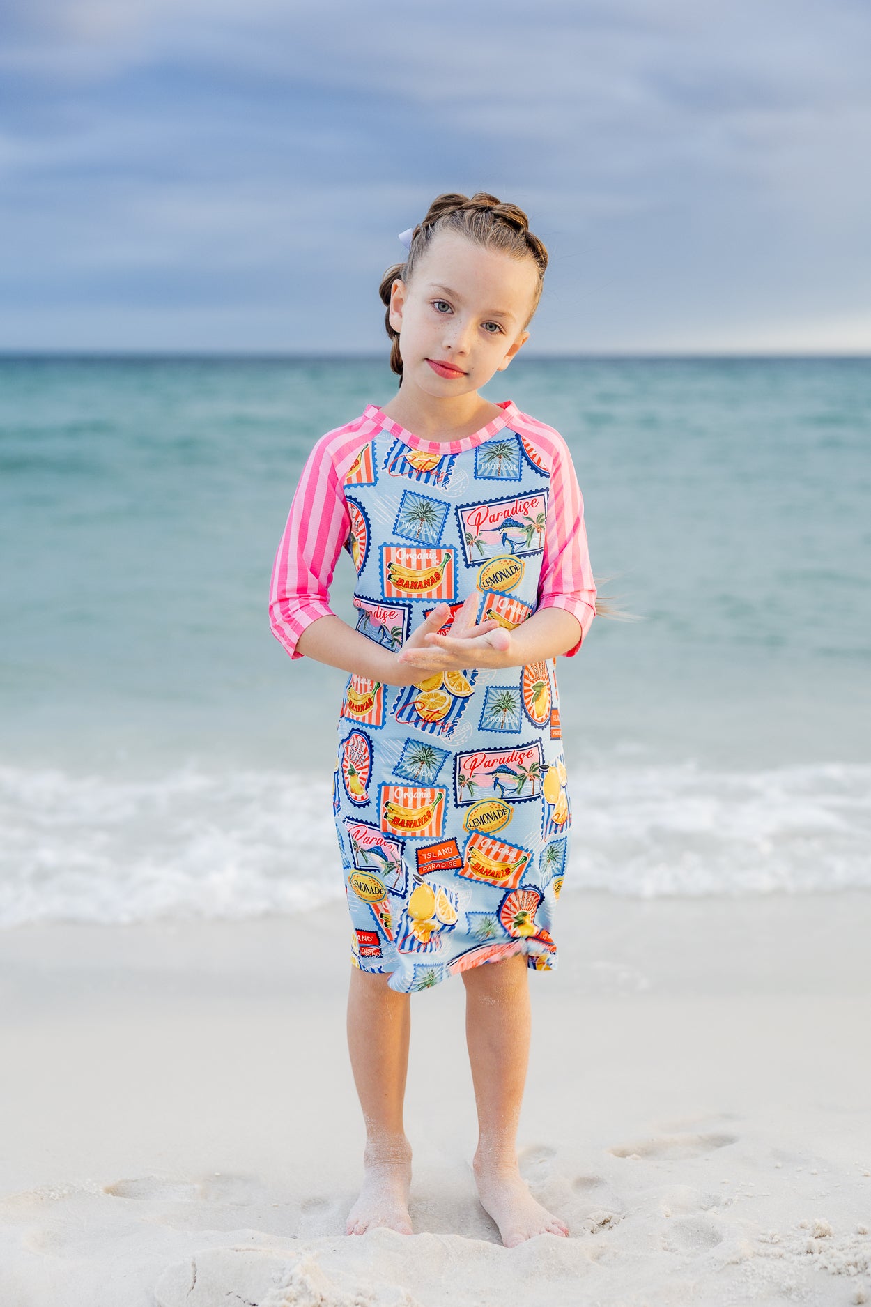 Model wearing Nuggles® Girls' Sport Swim Dress in Vacation Postcards