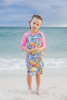 Model wearing Nuggles® Girls' Sport Swim Dress in Vacation Postcards