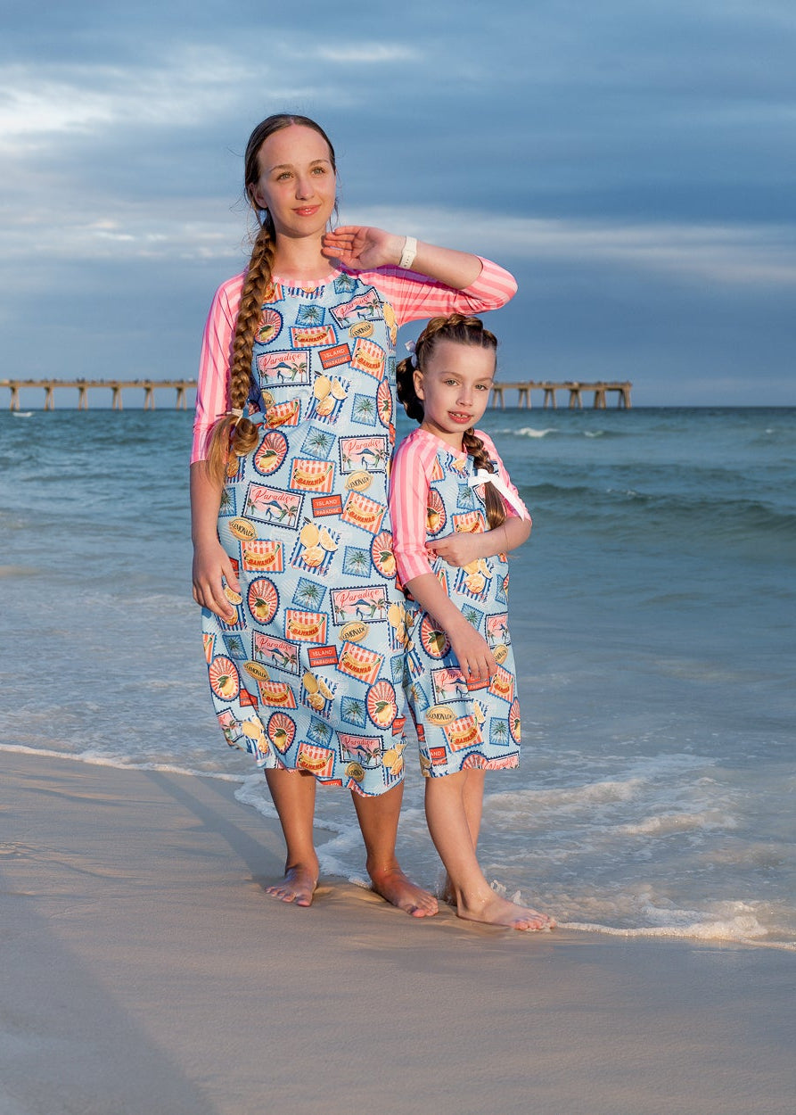 Model wearing Nuggles® Sport Swim Dress in Vacation Postcards