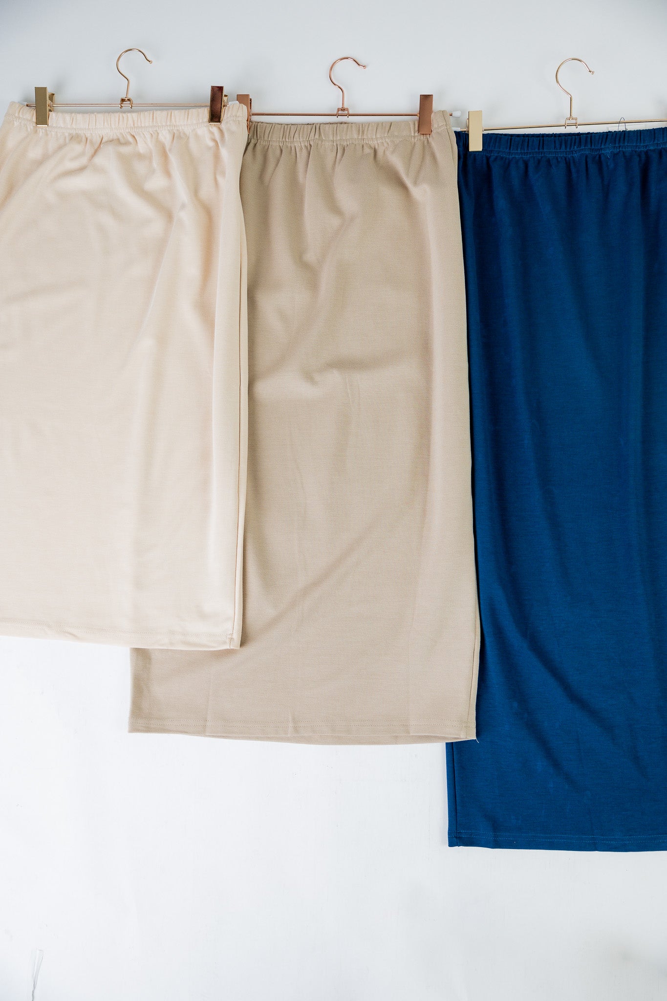 Two skirts, one beige and one blue, hanging on a rack against a white background.