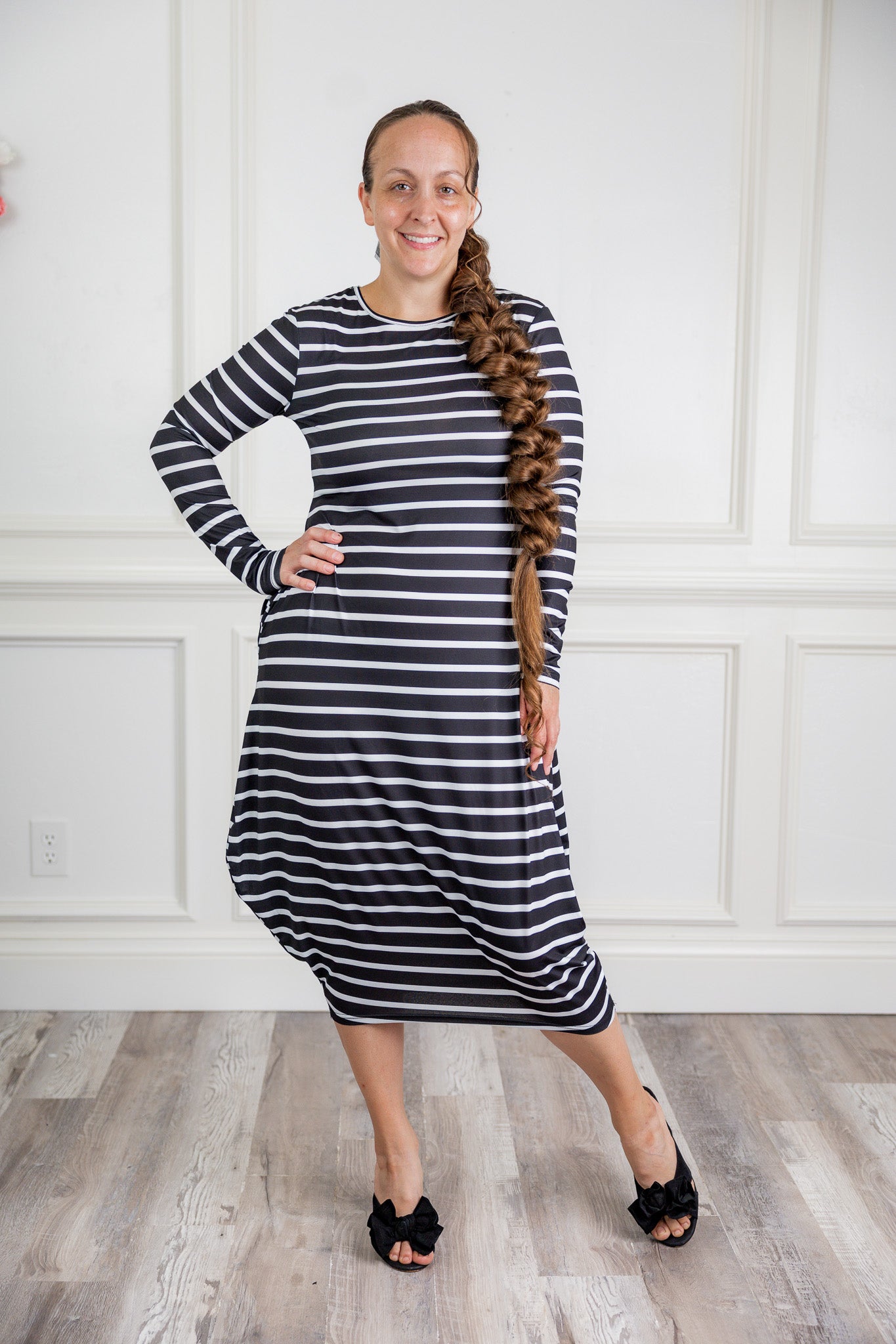 Woman modeling a Nuggles black and white stripe midi dress made from soft, stretchy knit fabric, featuring long sleeves and side pockets.