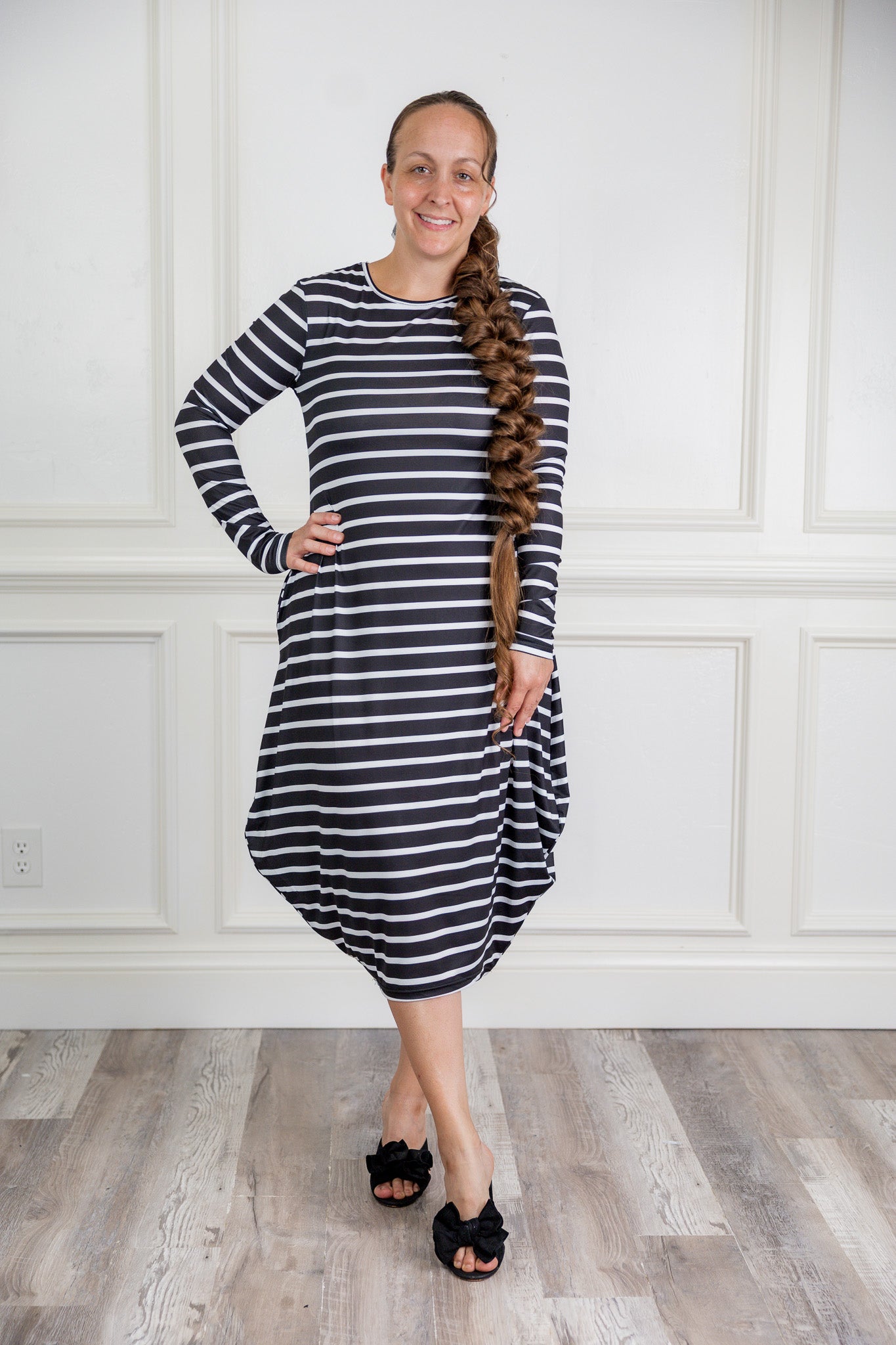 Woman modeling a Nuggles black and white stripe midi dress made from soft, stretchy knit fabric, featuring long sleeves and side pockets.