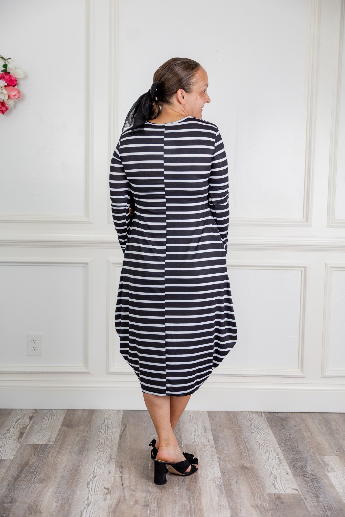 Woman modeling a Nuggles black and white stripe midi dress made from soft, stretchy knit fabric, featuring long sleeves and side pockets.