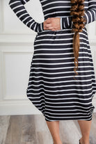 Woman modeling a Nuggles black and white stripe midi dress made from soft, stretchy knit fabric, featuring long sleeves and side pockets.