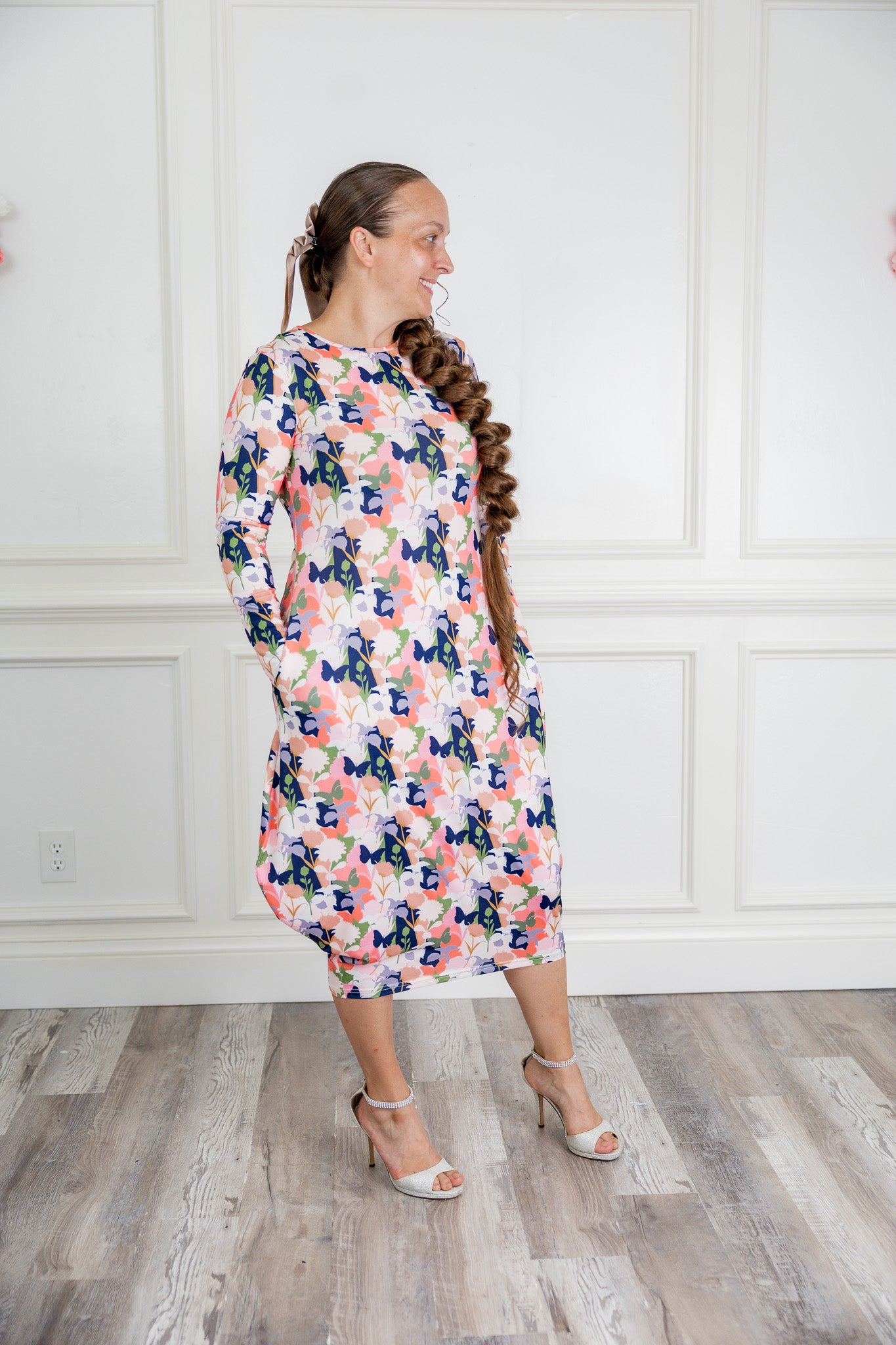 Woman modeling a Nuggles floral print midi dress made from soft, stretchy knit fabric, featuring long sleeves and side pockets.