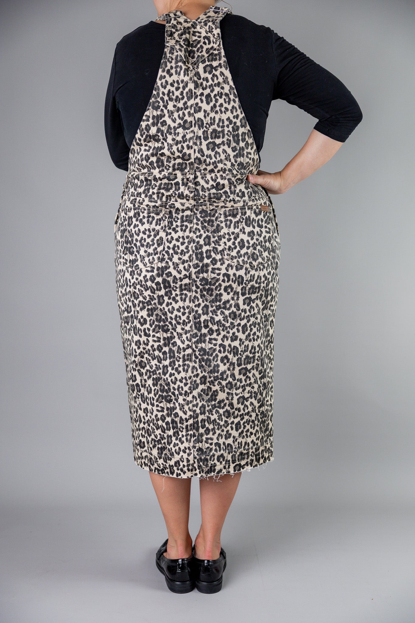 Model wearing a 'NUGGLES® modest leopard denim overall dress with front pocket and raw hem.