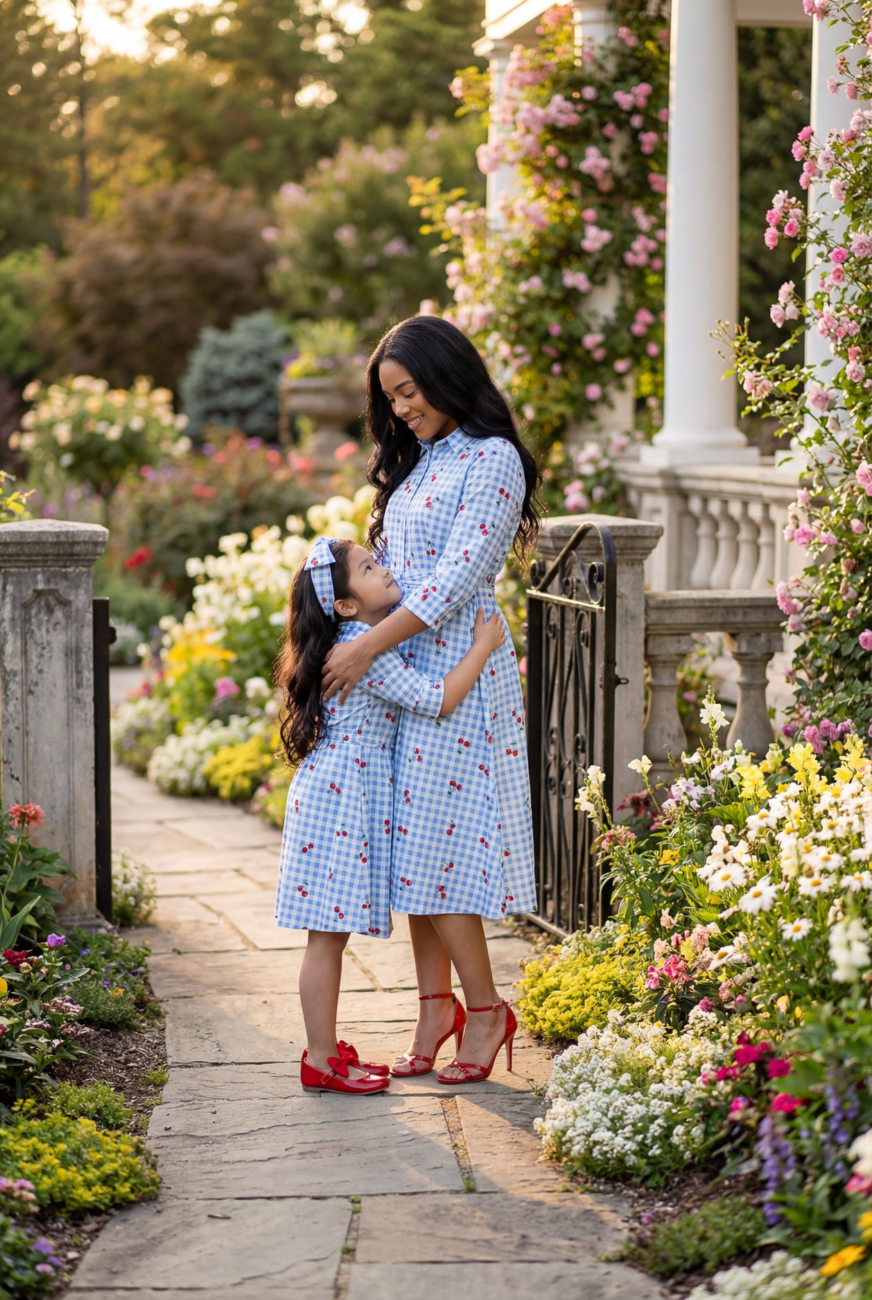 Woman and child in matching blue checkered dresses standing in a garden.