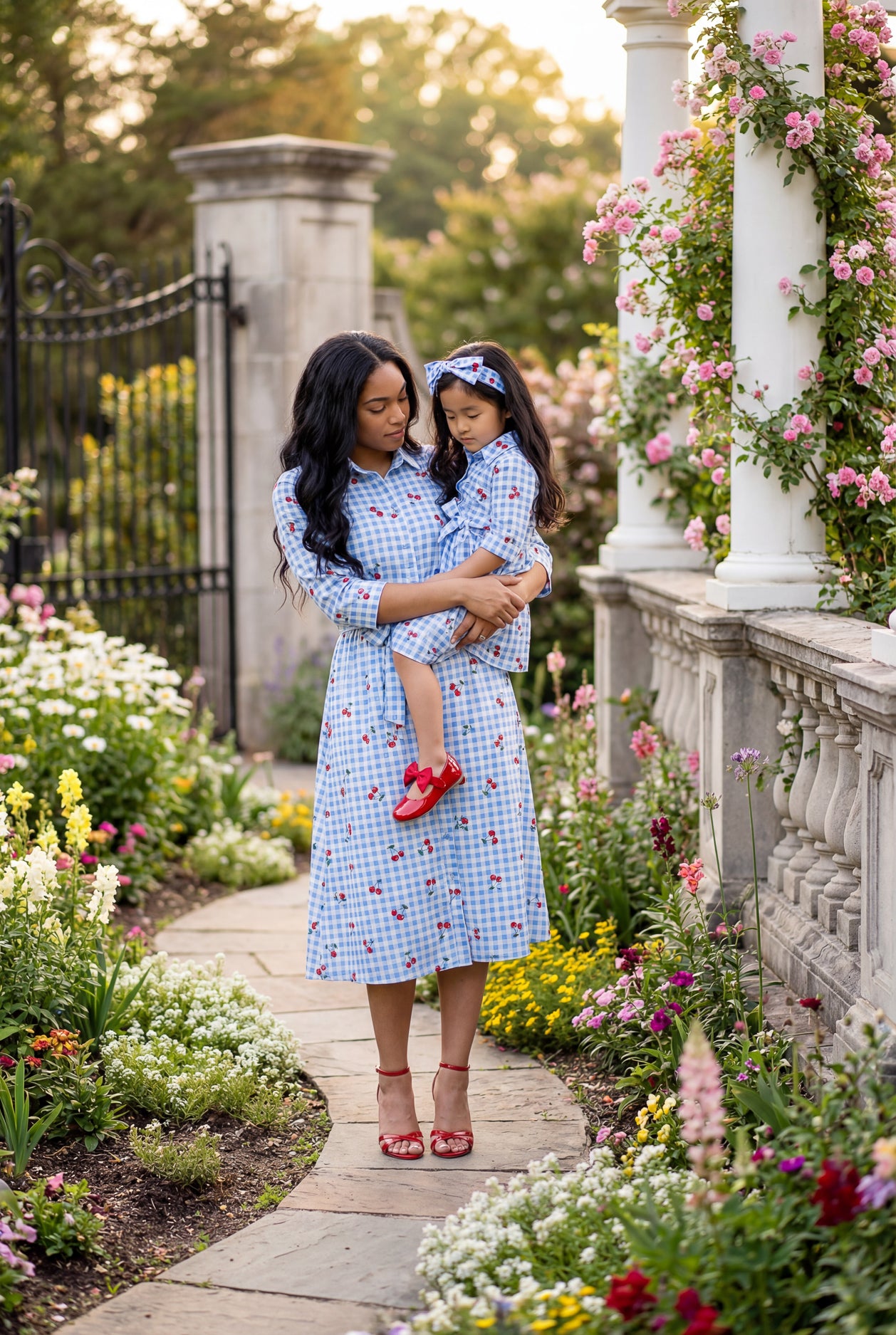 Woman and child in matching blue checkered dresses standing in a garden.