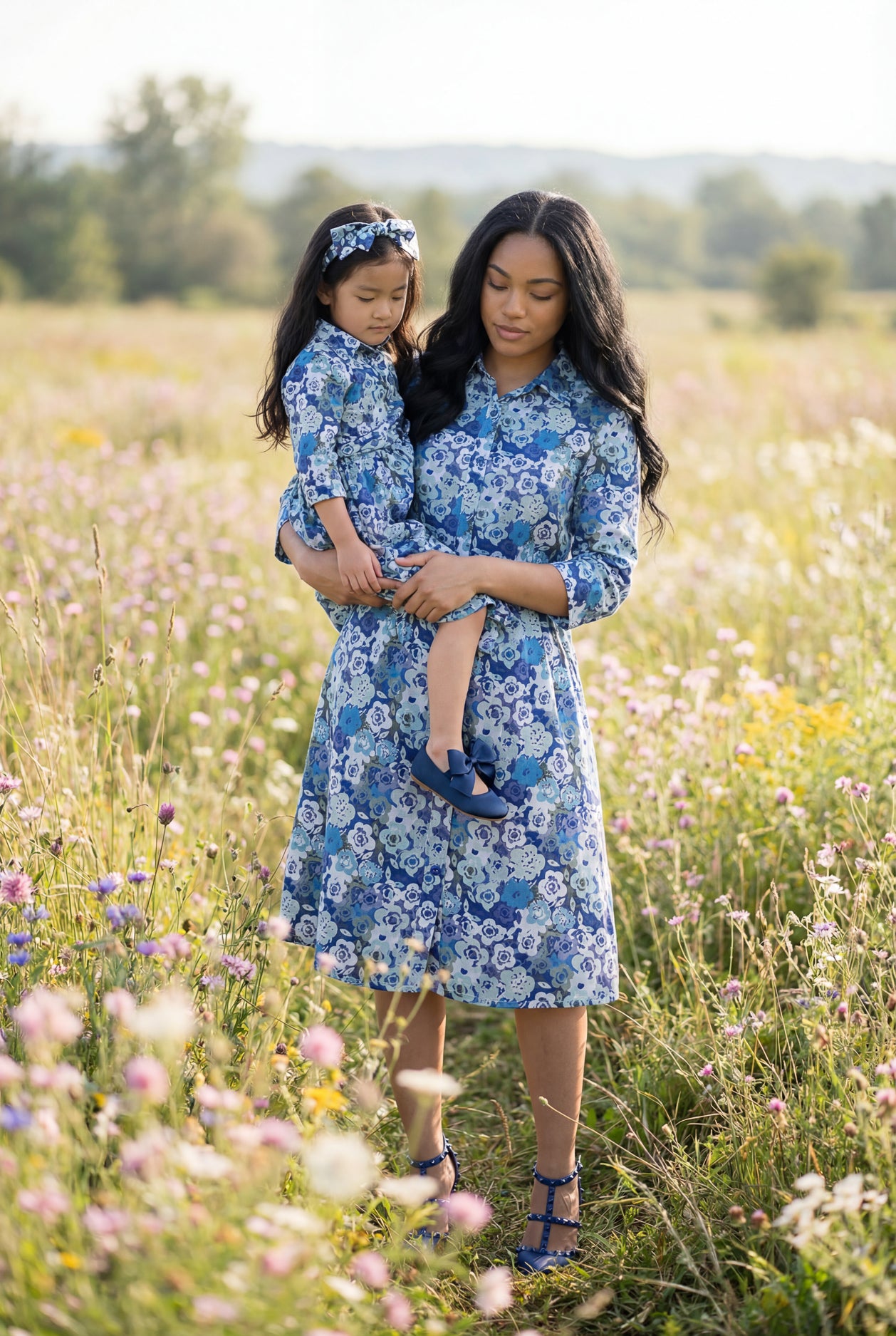 Woman and child in matching blue floral dresses standing in a field of wildflowers.