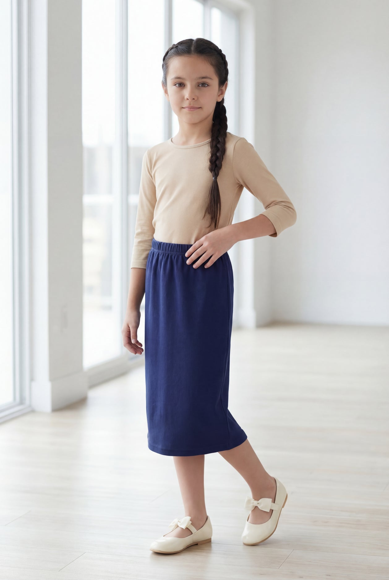 Young girl wearing a modest midi length skirt in navy with a beige colored 3/4 length sleeve shirt. 