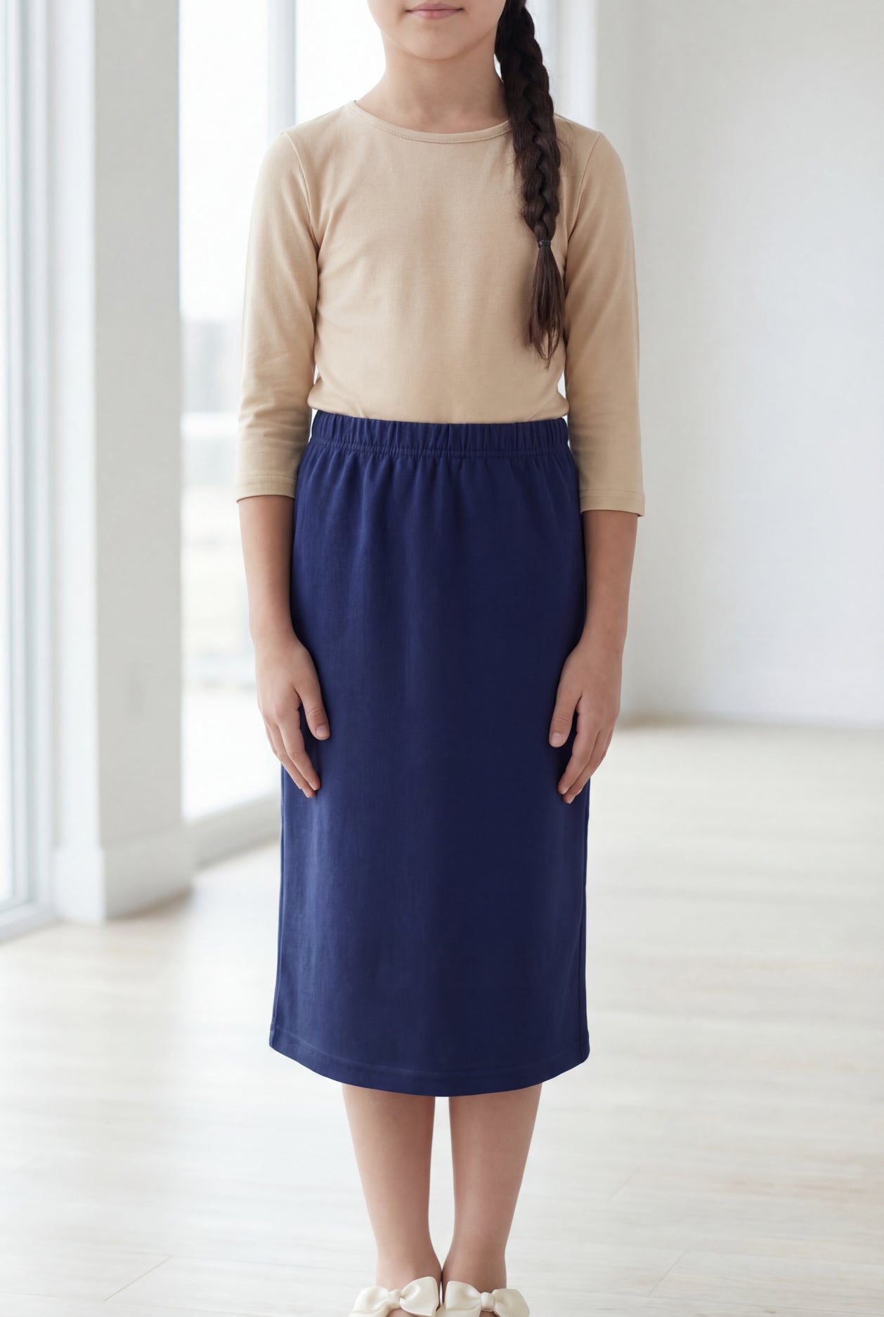 Young girl wearing a modest midi length skirt in navy with a beige colored 3/4 length sleeve shirt. 