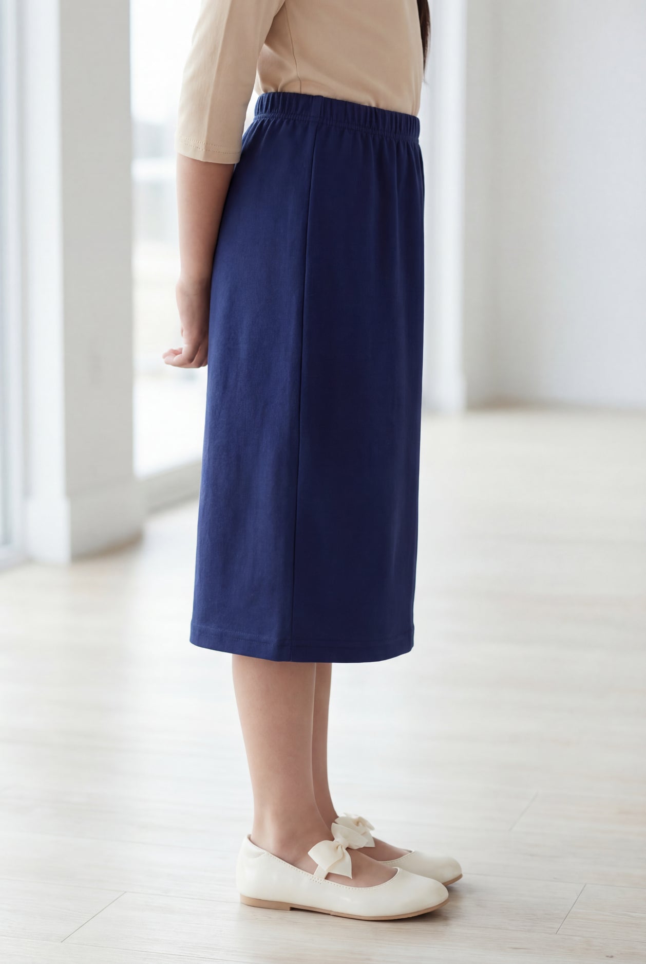 Young girl wearing a modest midi length skirt in navy with a beige colored 3/4 length sleeve shirt. 
