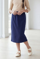 Young girl wearing a modest midi length skirt in navy with a beige colored 3/4 length sleeve shirt. 