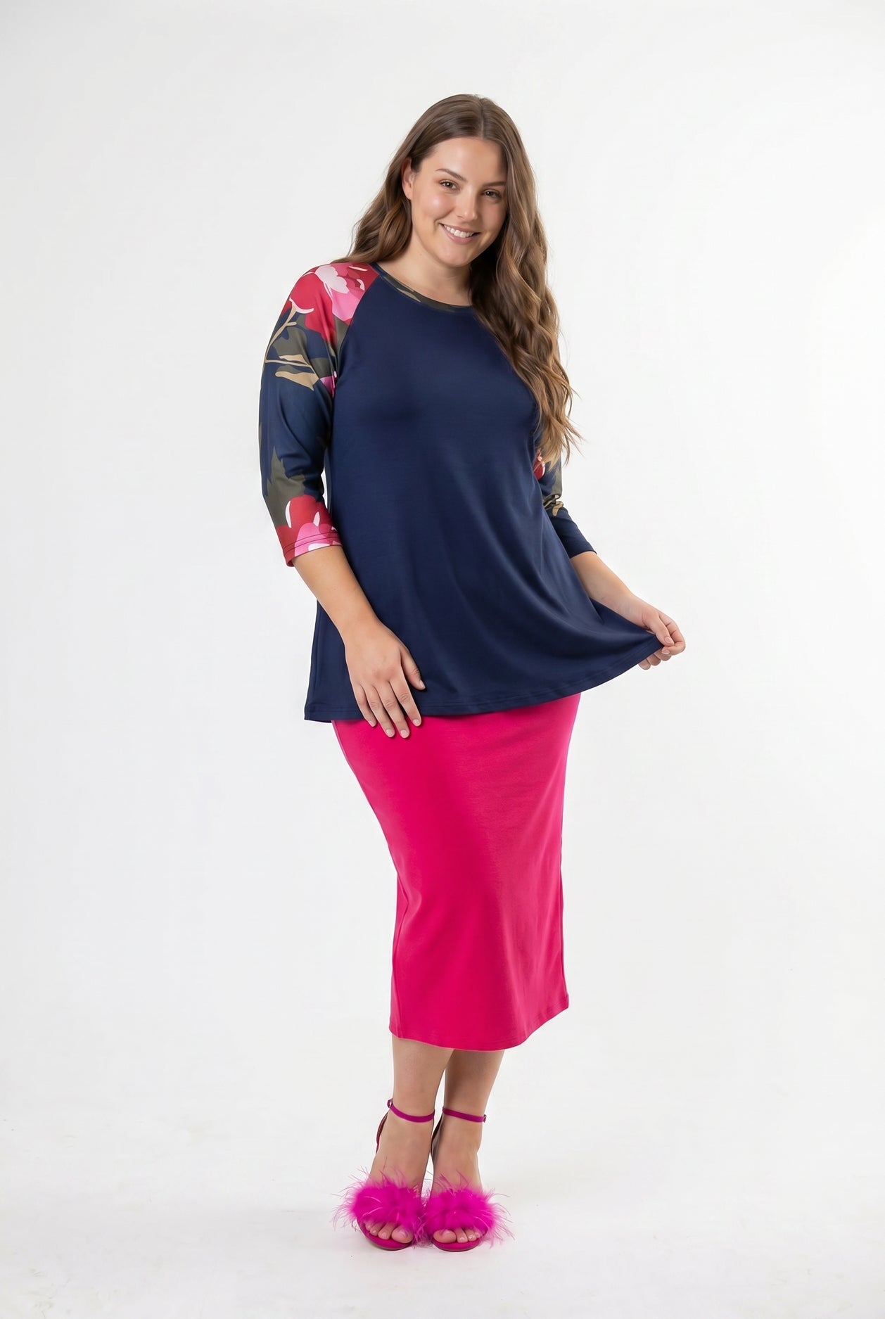 Woman modeling a navy floral-sleeve top with a bright pink skirt and matching pink heels against a clean white studio background.