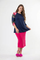 Woman modeling a navy floral-sleeve top with a bright pink skirt and matching pink heels against a clean white studio background.