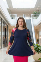 Woman modeling a navy floral-sleeve top in a mall.