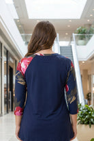 Woman modeling a navy floral-sleeve top in a mall.