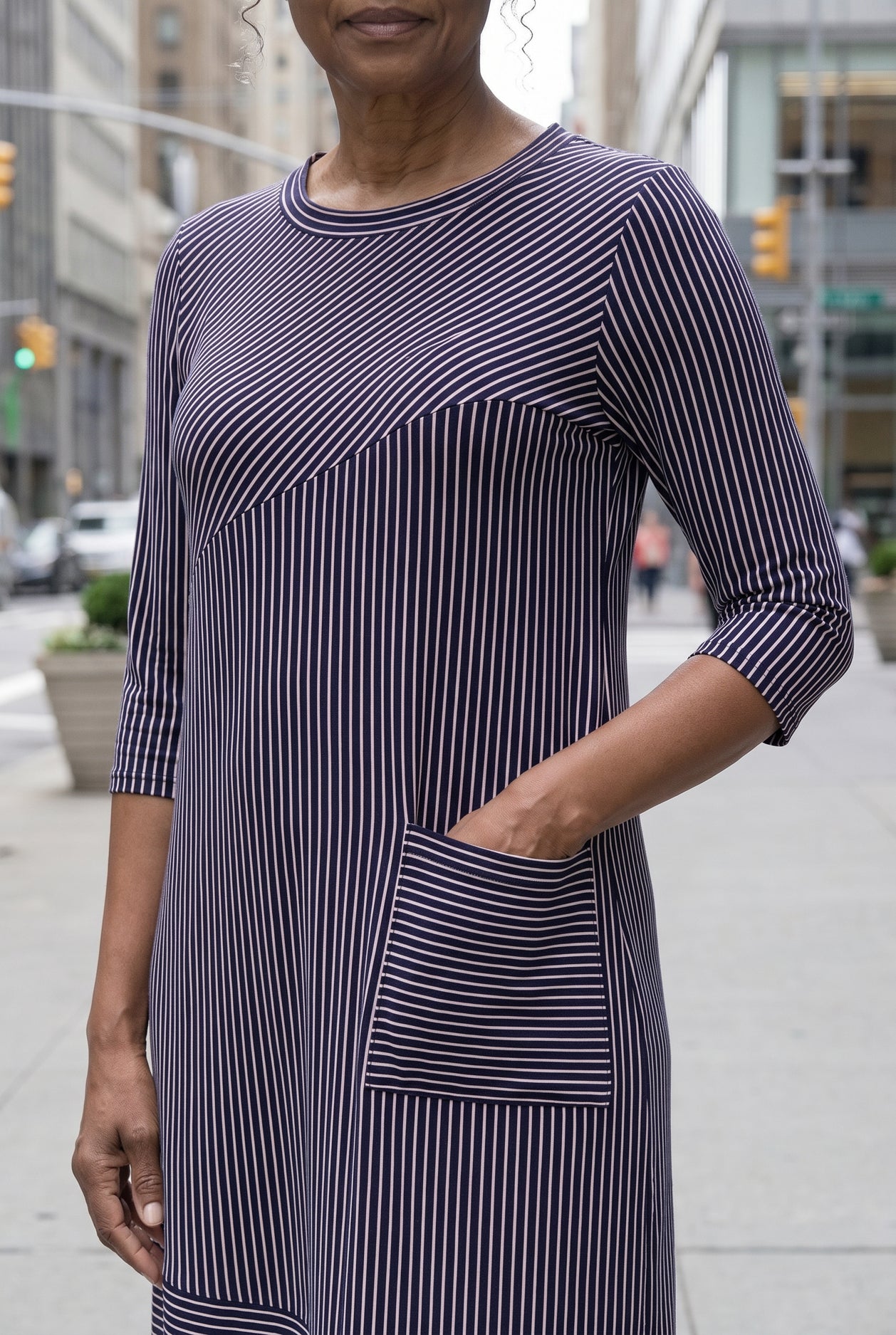 Women standing in a navy and pink stripe dress on a busy city street. 