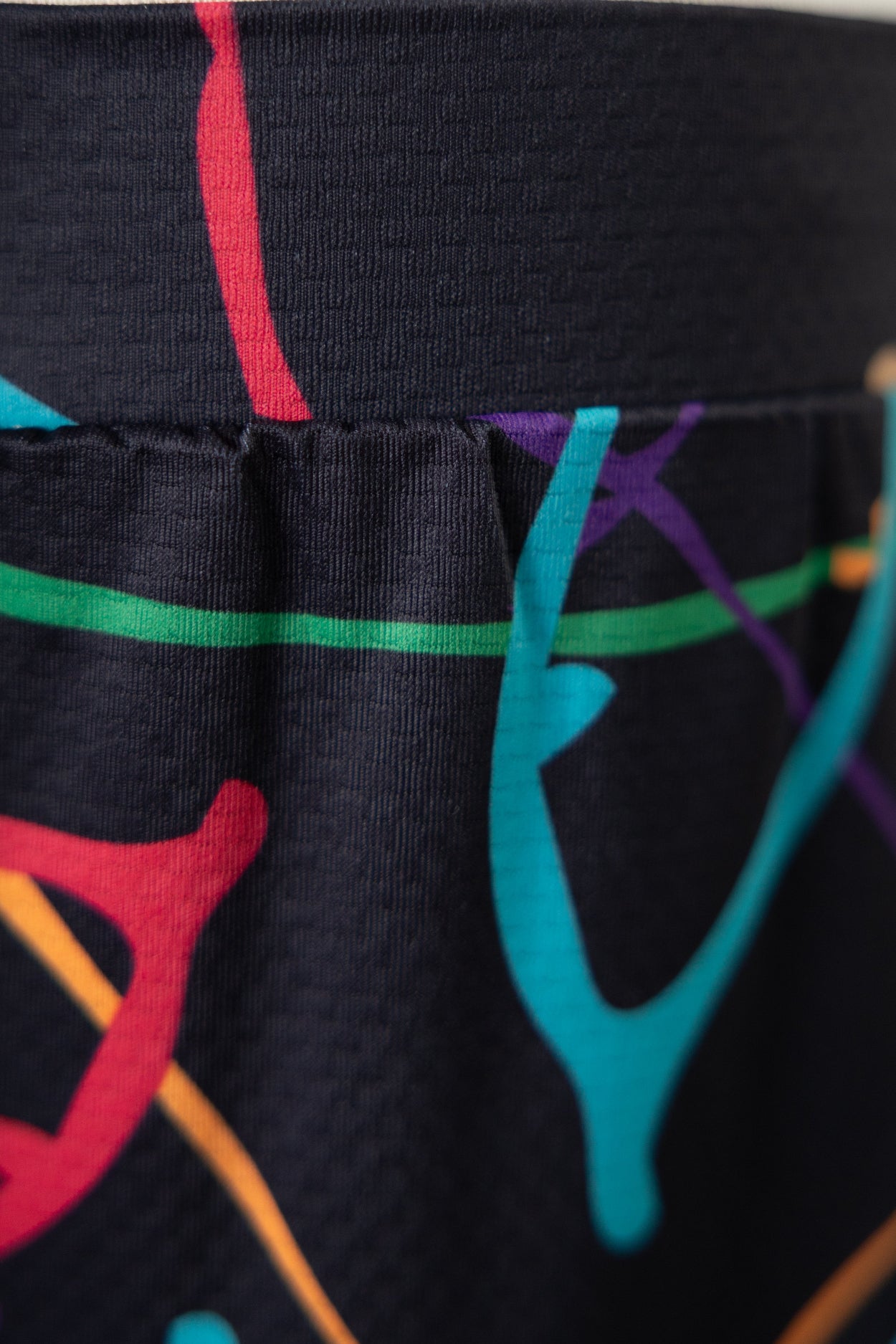 Close-up of black leggings with colorful abstract designs on a plain background