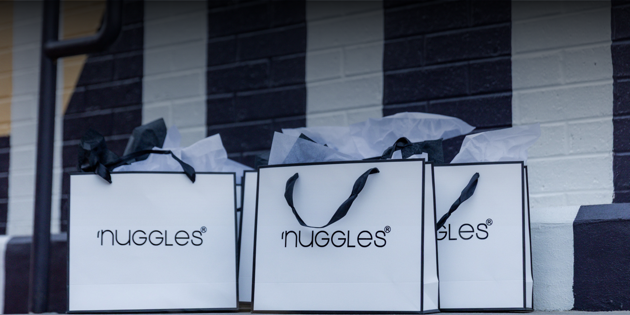 Three 'Nuggles' branded shopping bags against a striped wall.