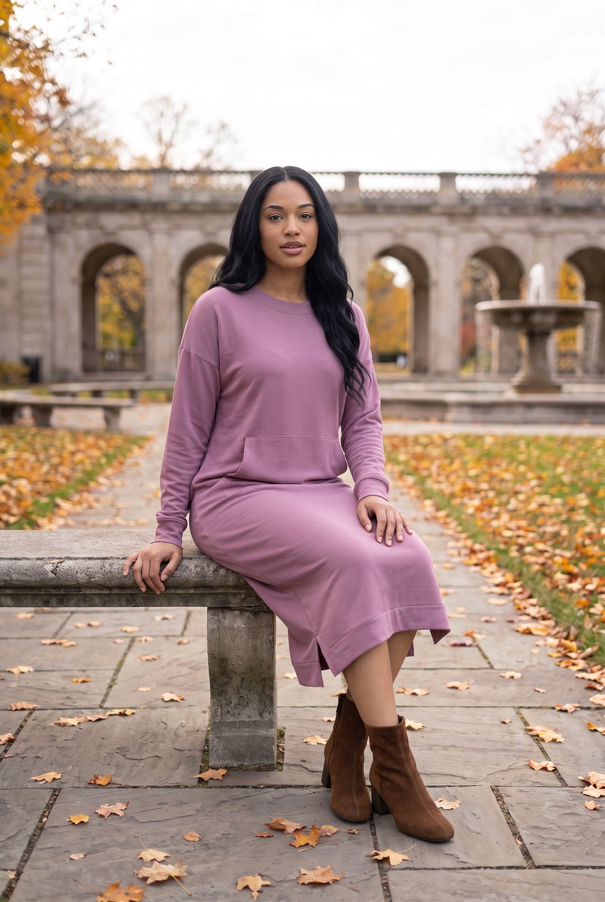 Nuggles® Oakley Hoodie Dress in Pale Purple, seated sideways on a stone bench along a leaf-lined walkway