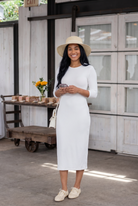 Woman in a white dress and hat standing in front of a rustic wooden door.