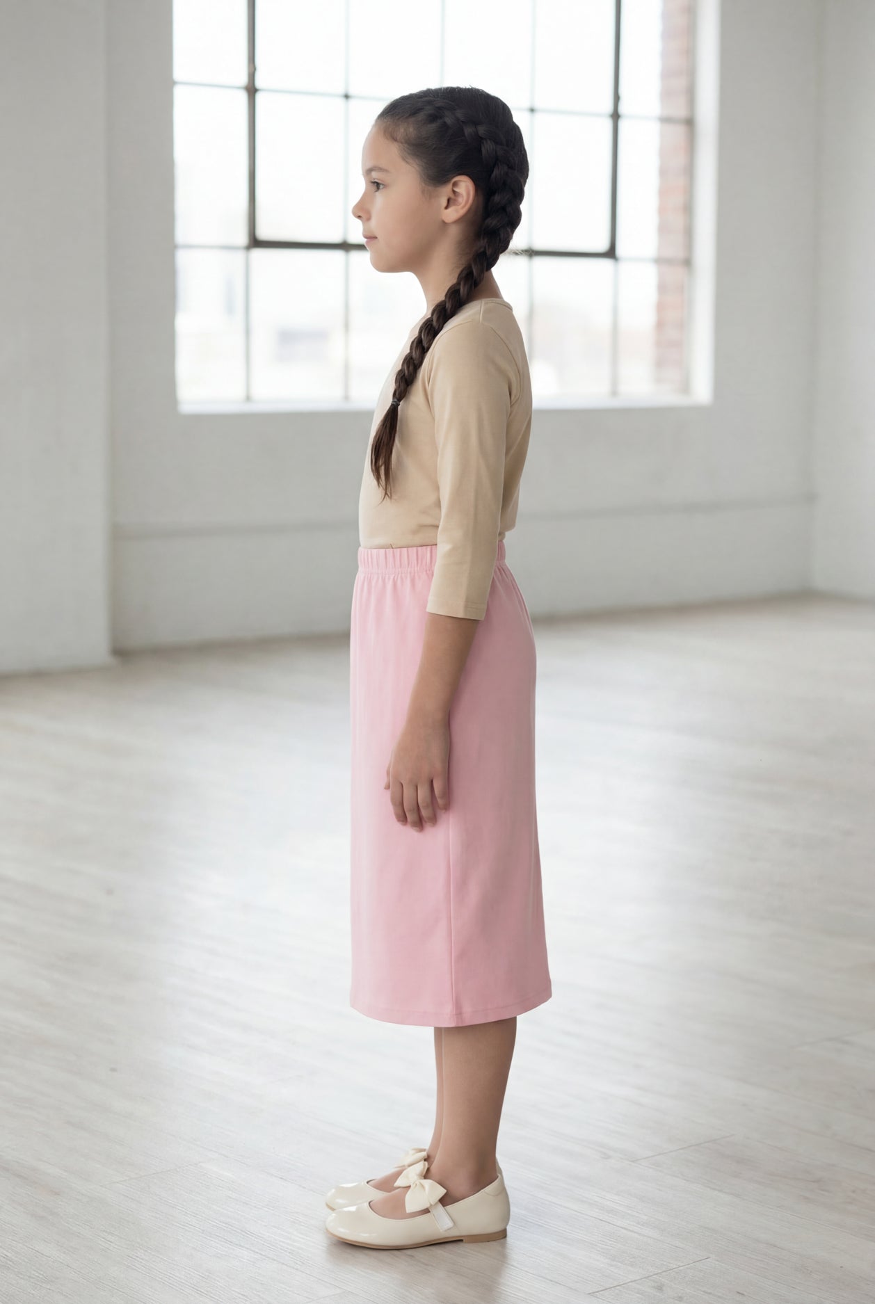 Girl wearing a Nuggles® blush midi length classic skirt with a 3/4 sleeve length soft tee in a sunlight loft. 