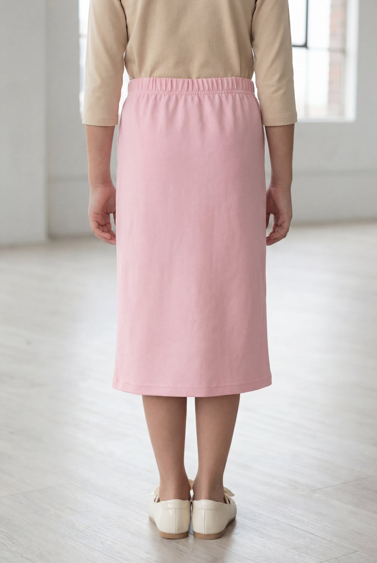 Girl wearing a Nuggles® blush midi length classic skirt with a 3/4 sleeve length soft tee in a sunlight loft. 