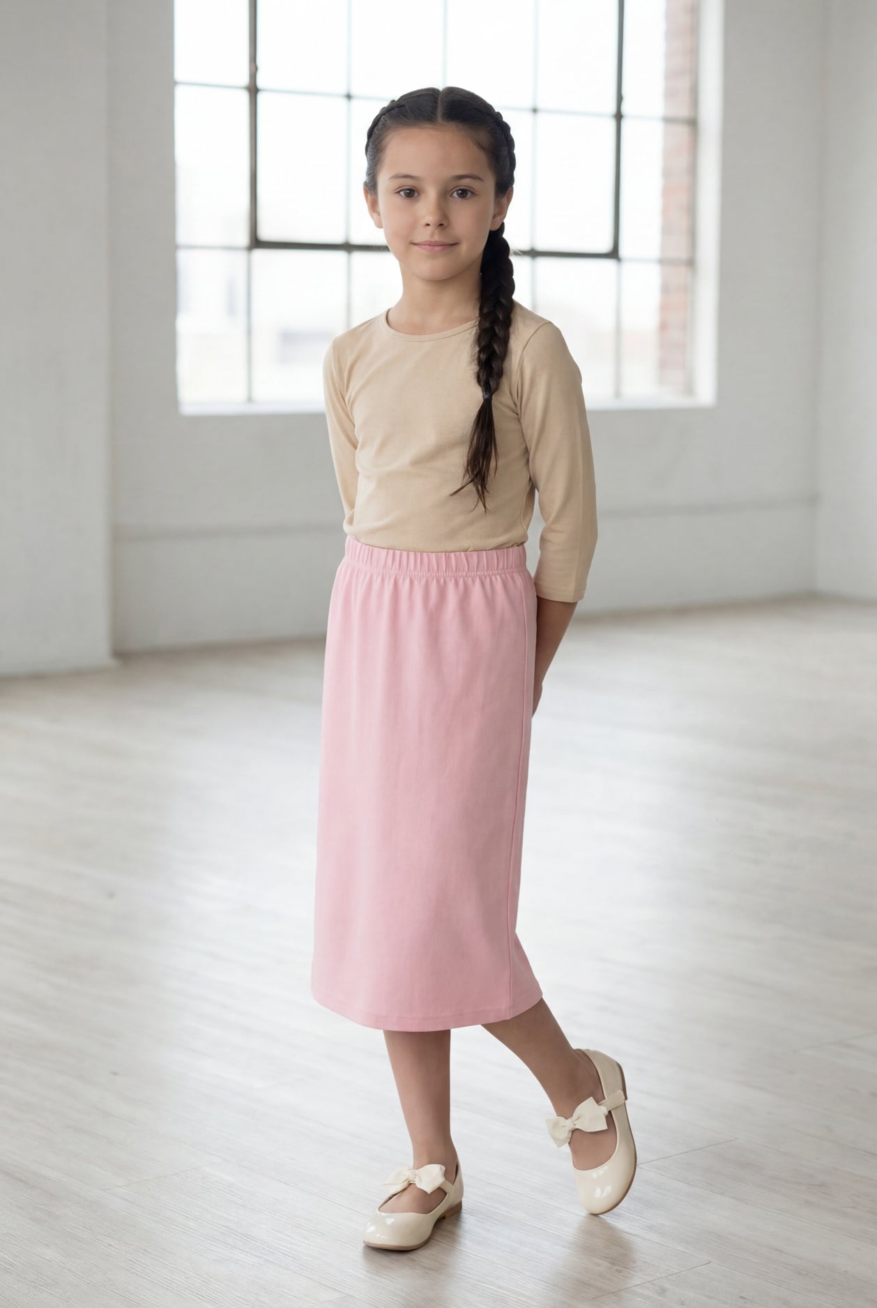 Girl wearing a Nuggles® blush midi length classic skirt with a 3/4 sleeve length soft tee in a sunlight loft. 