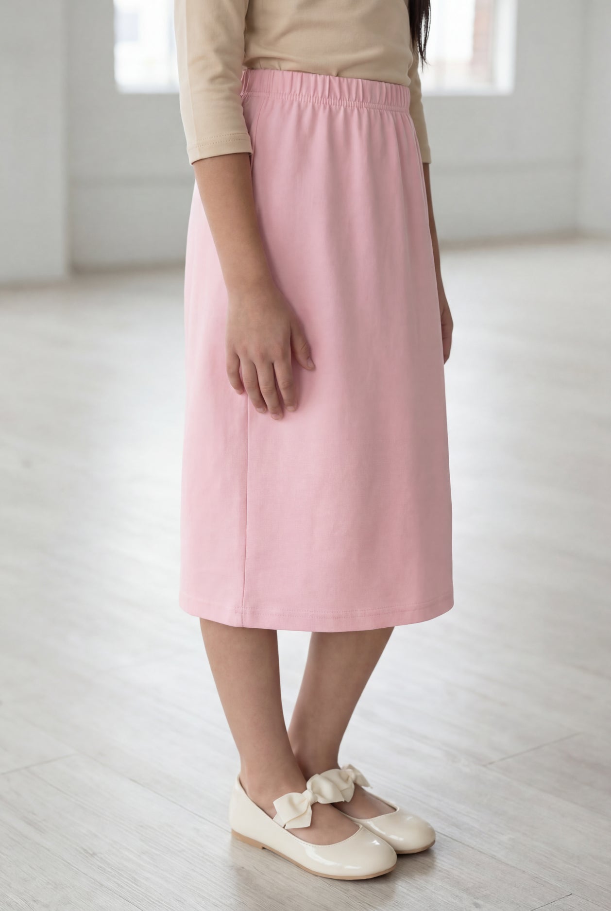 Girl wearing a Nuggles® blush midi length classic skirt with a 3/4 sleeve length soft tee in a sunlight loft. 